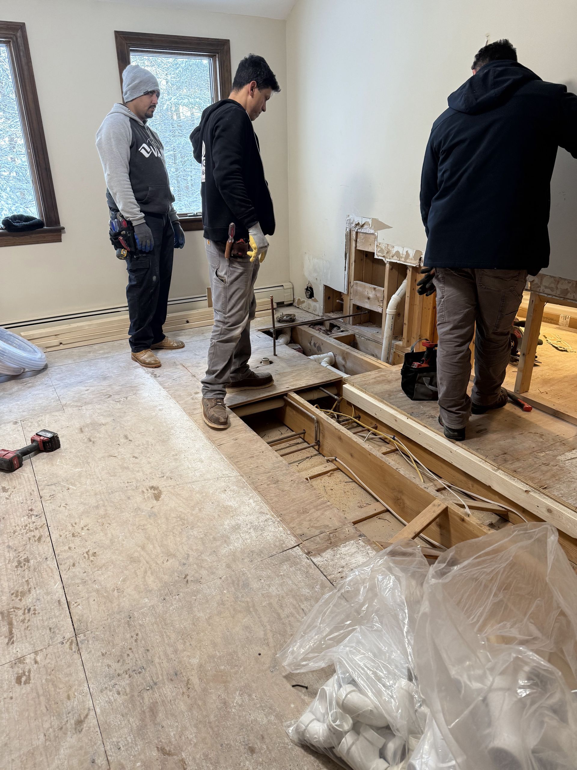 Three workers renovating a room, removing flooring and working near a window.