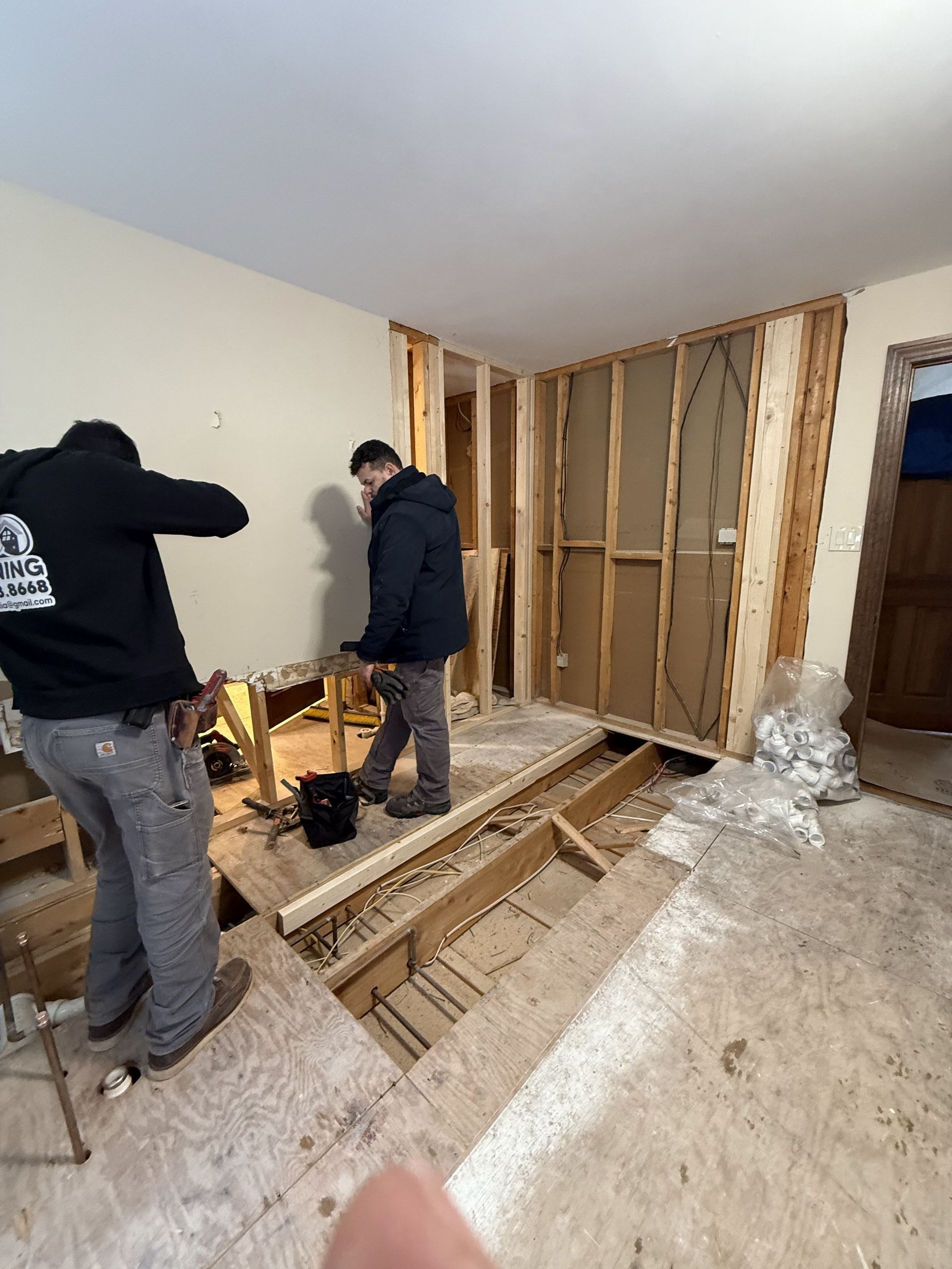 Two people renovating a room; exposed framing, hole in floor, one person holds a tool.