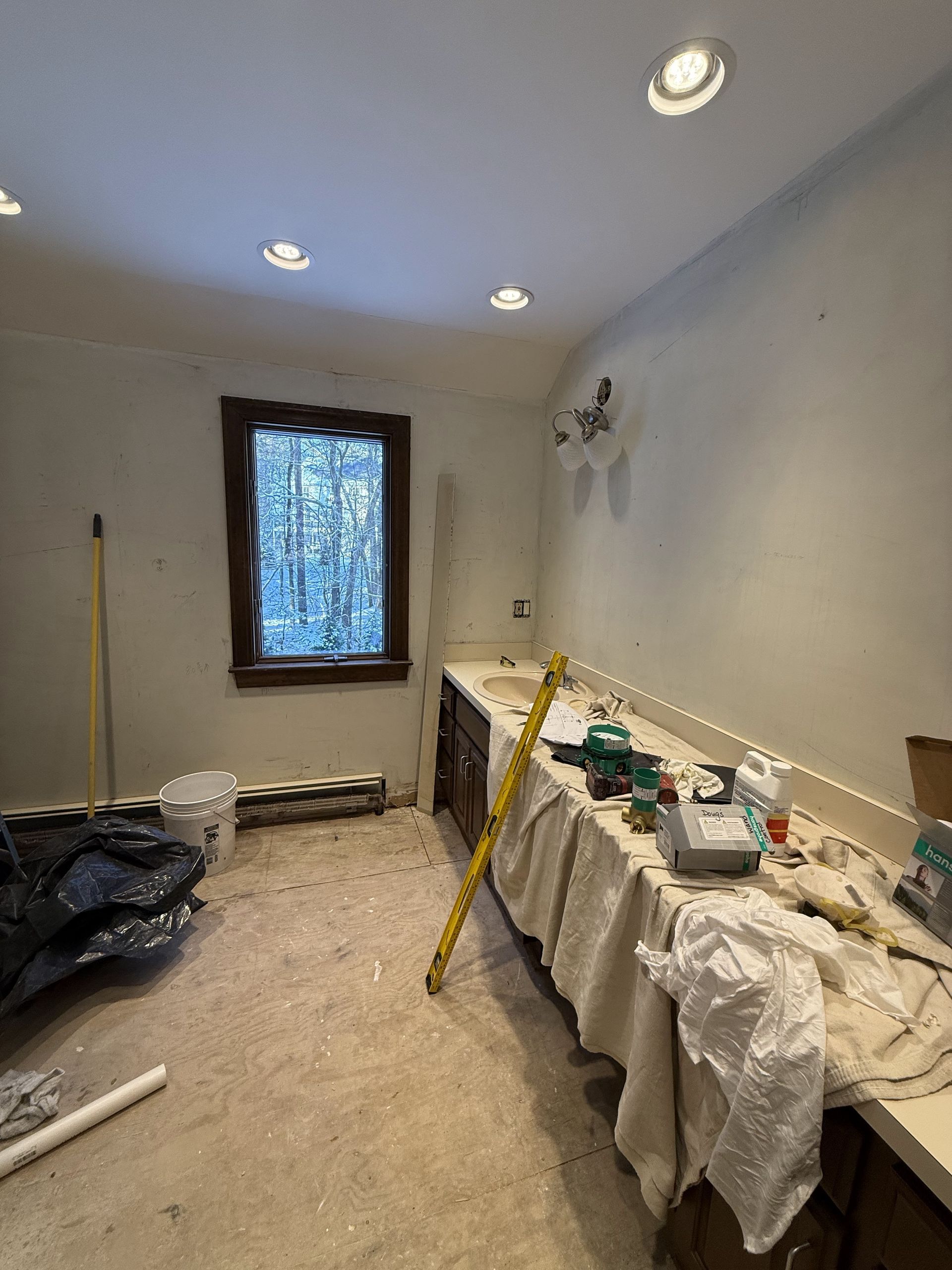 Interior view of a room under renovation. Counter with tools, window with a wooden frame, bare walls, and recessed lighting.