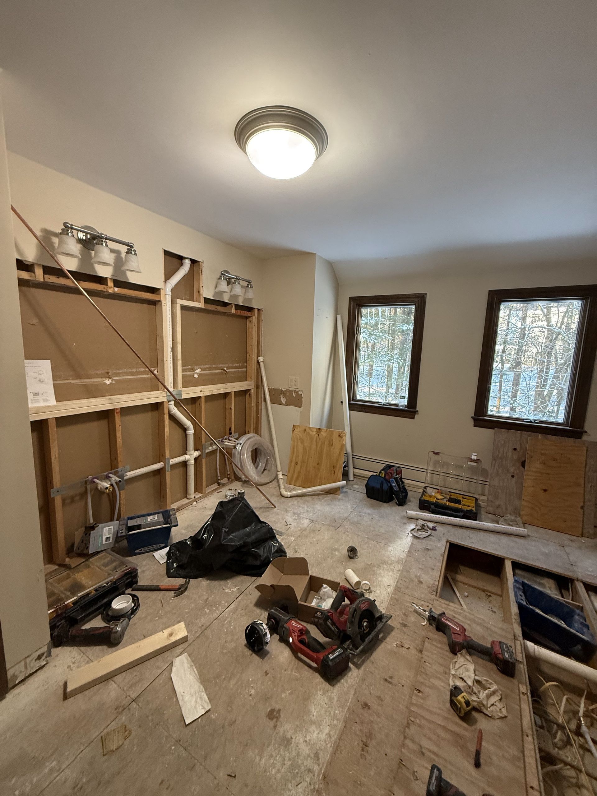 Room under renovation, tools and materials scattered, walls partially torn down, windows on the right.