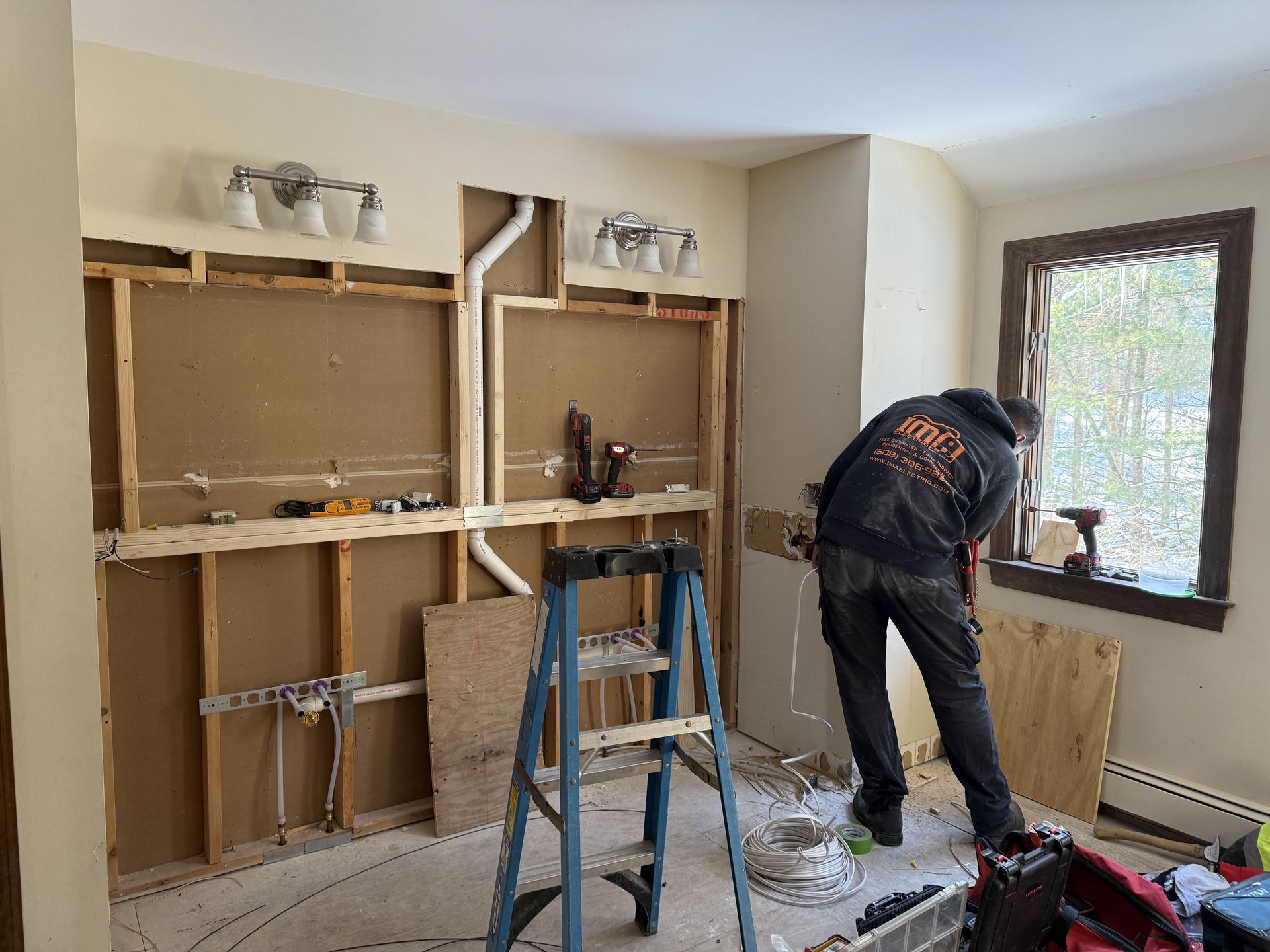 Man working on a bathroom remodel. Walls are open, showing plumbing and framing. A ladder is in the foreground.