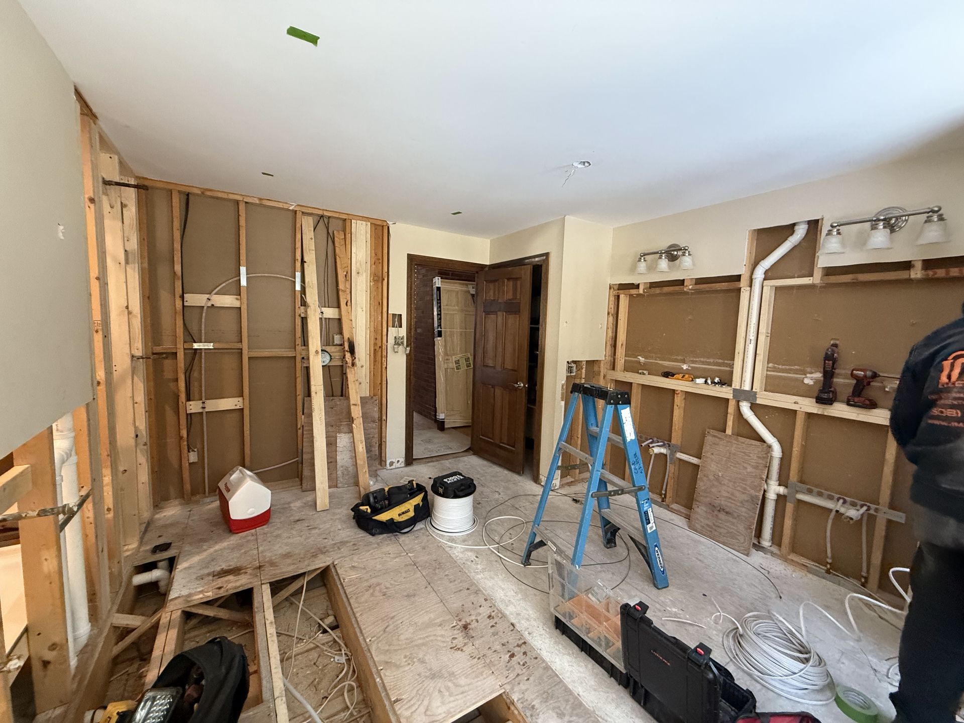 Room under renovation; exposed studs, drywall removed, tools and debris on floor, door visible.