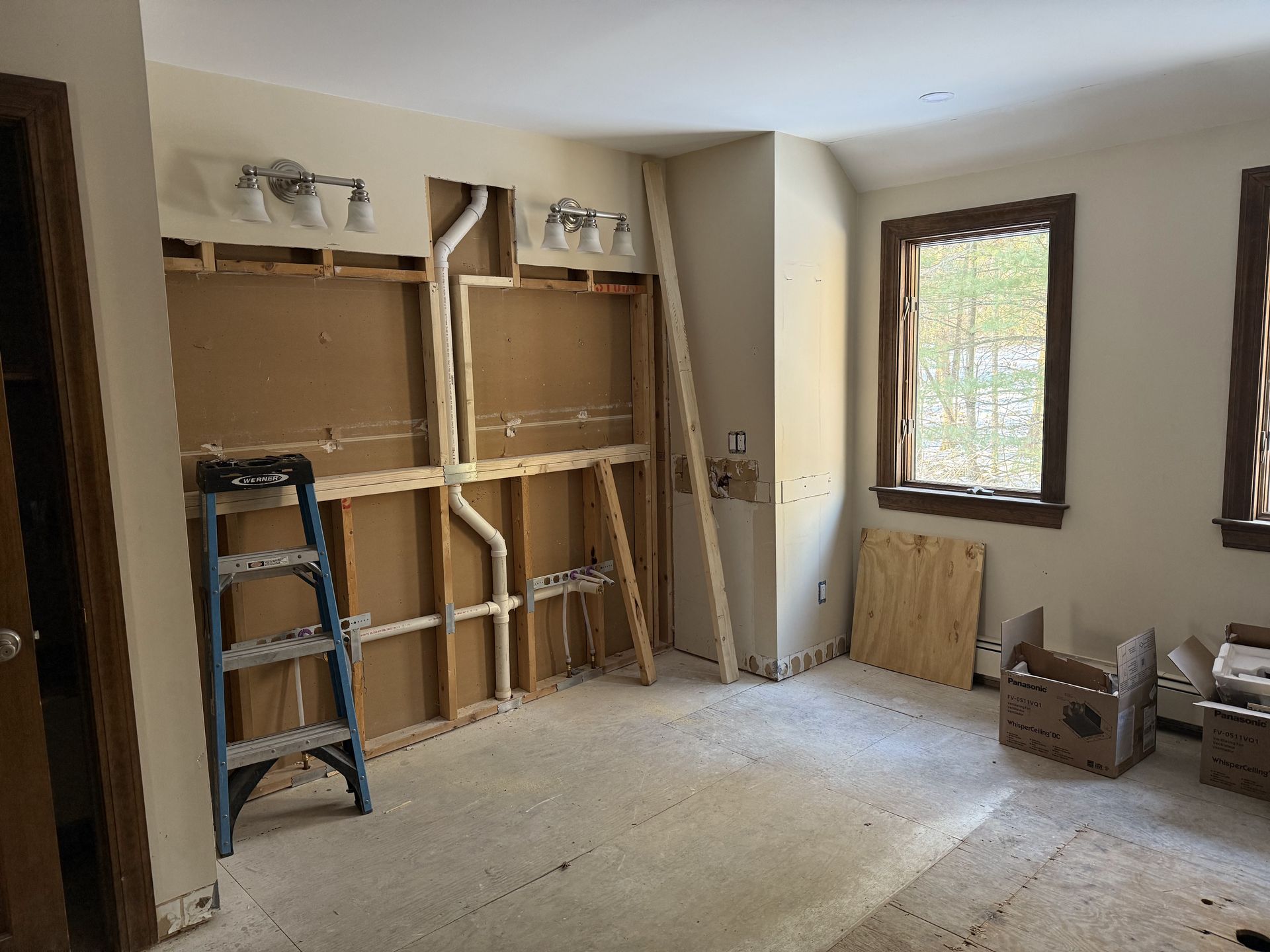 Bathroom under construction with exposed framing, pipes, and a ladder.