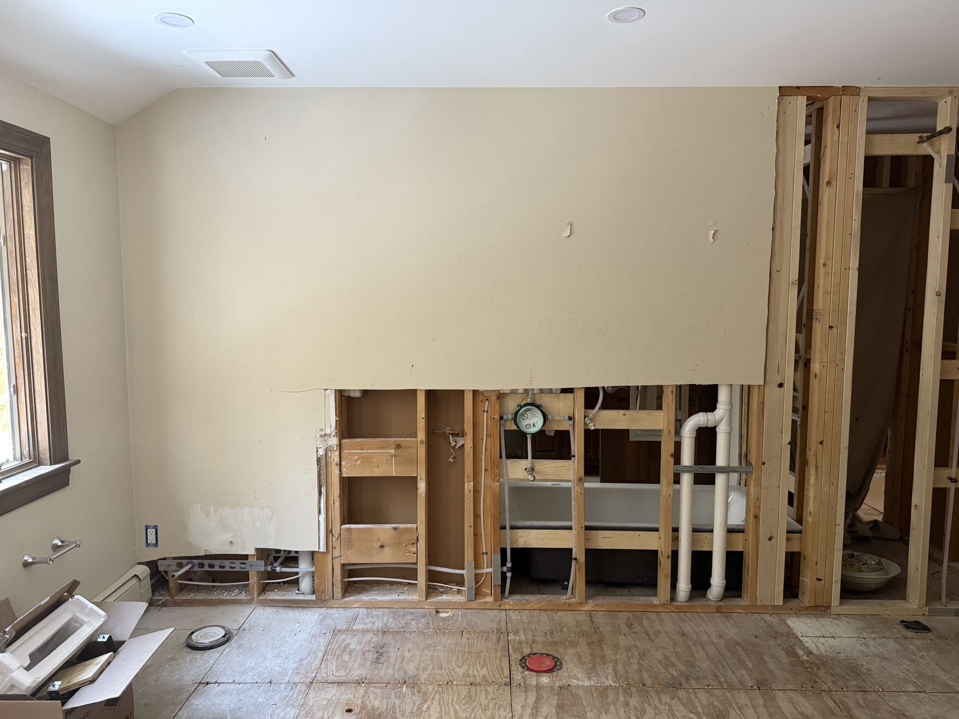 Interior wall under renovation, exposing plumbing and wooden framing.