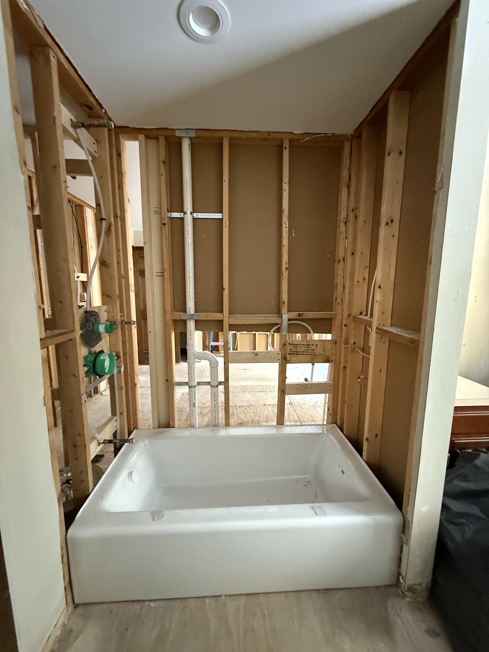 Bathroom renovation: a white bathtub installed in a framed-out alcove with exposed plumbing.