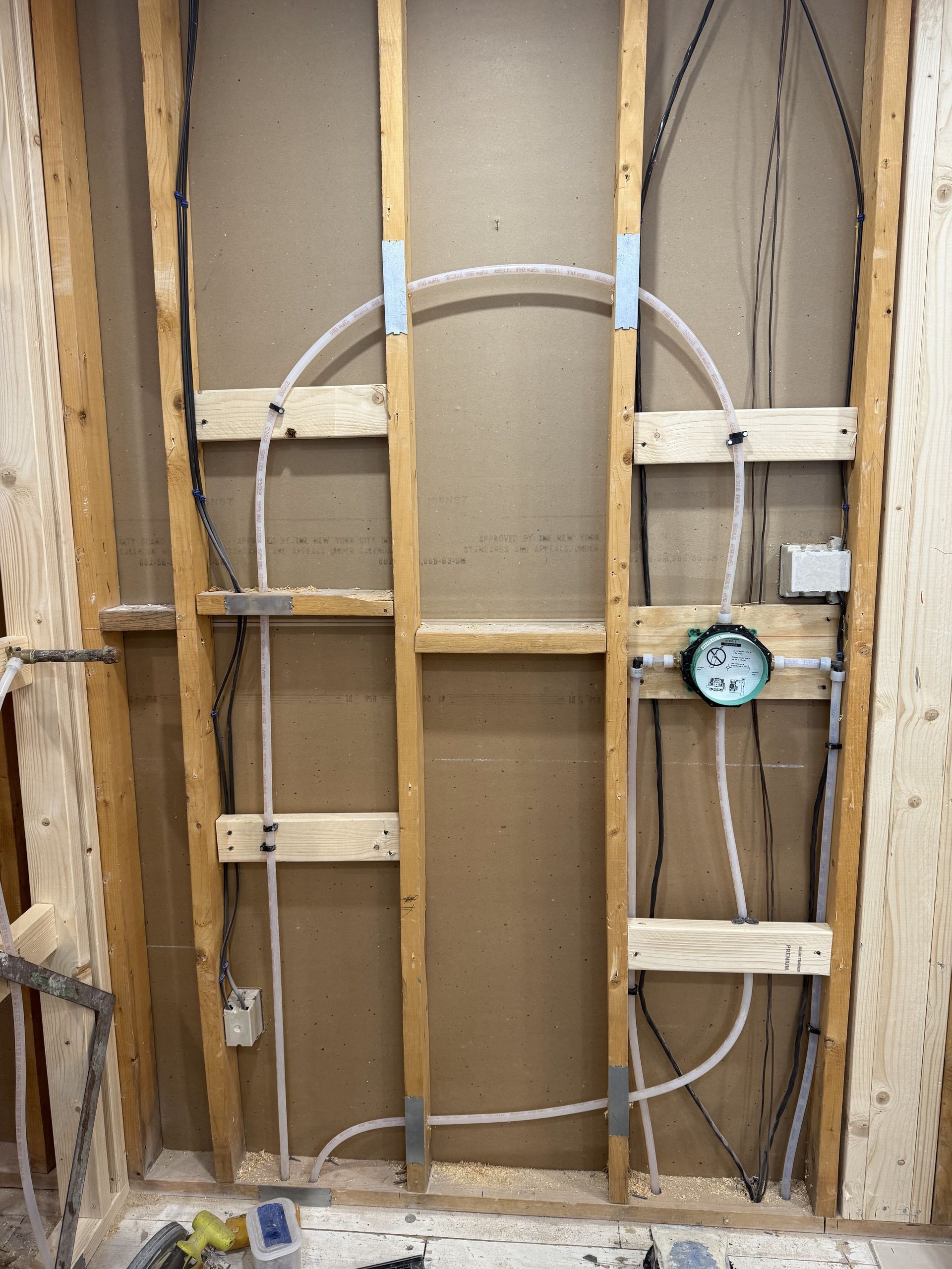 Interior wall framing with plumbing and electrical lines installed for a shower.