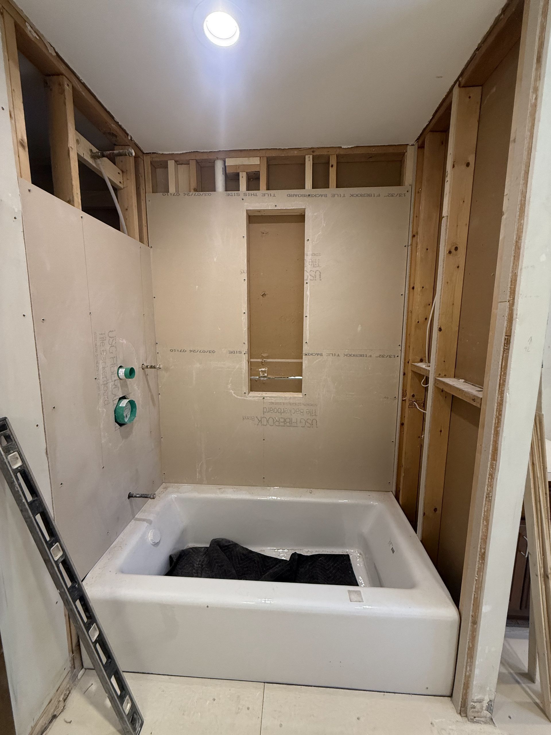 Bathroom renovation in progress: a white bathtub is installed, walls are framed, and waterproof drywall is partially up.