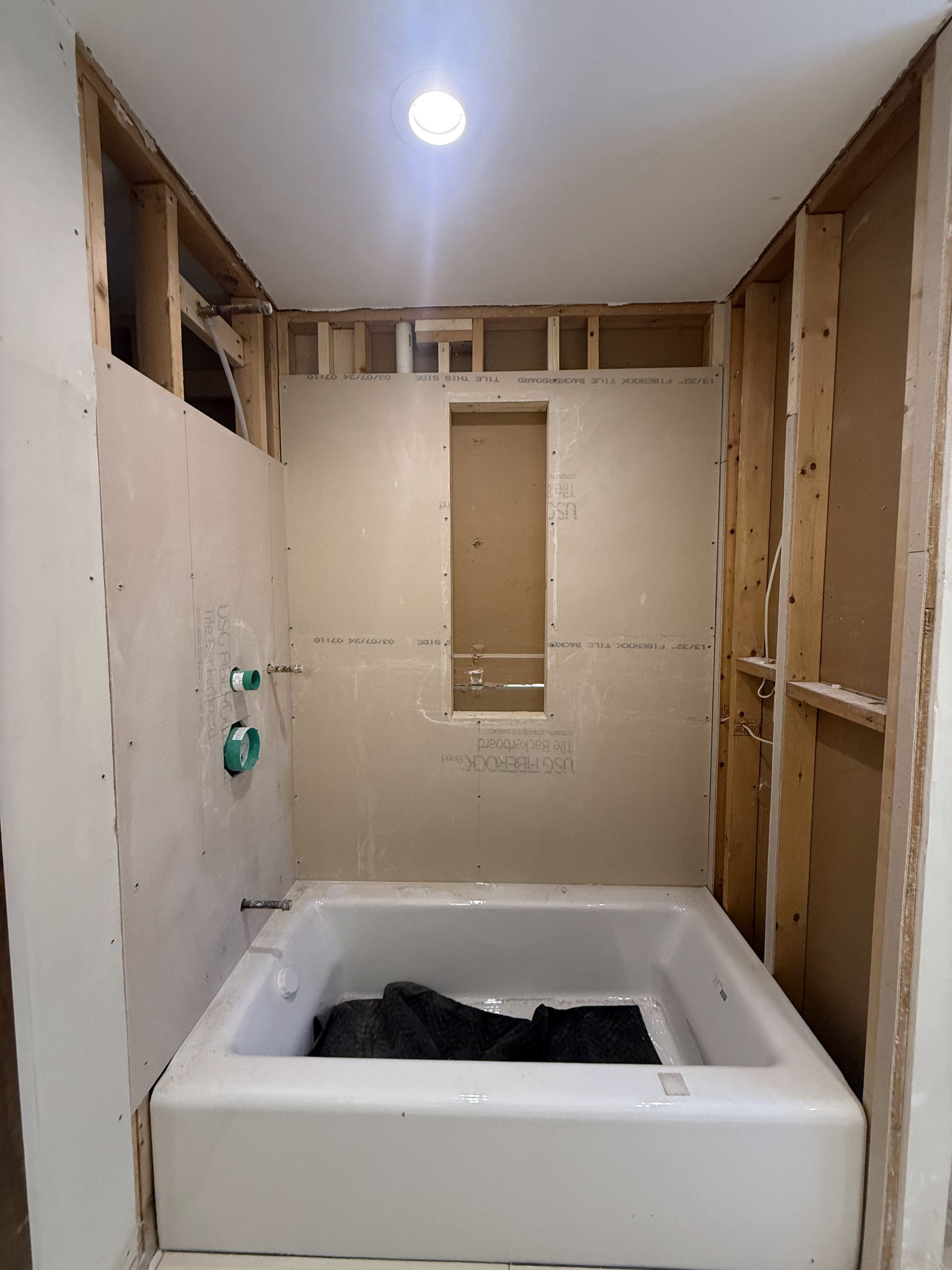 Bathroom renovation in progress: bathtub, exposed framing, partially installed wallboard, plumbing fixtures.
