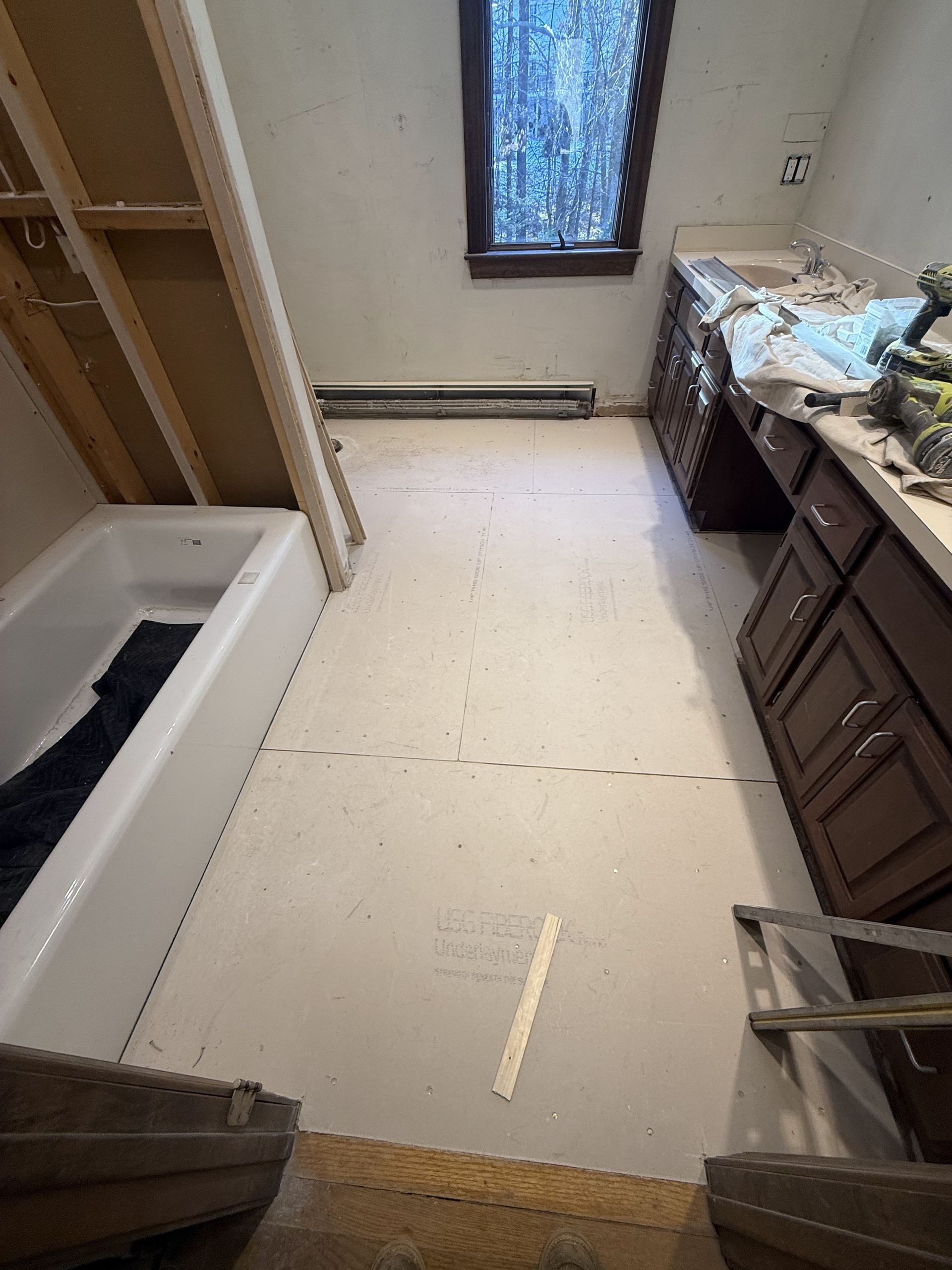 Bathroom under construction; white floor, brown cabinets, bathtub, window, and exposed wall studs.