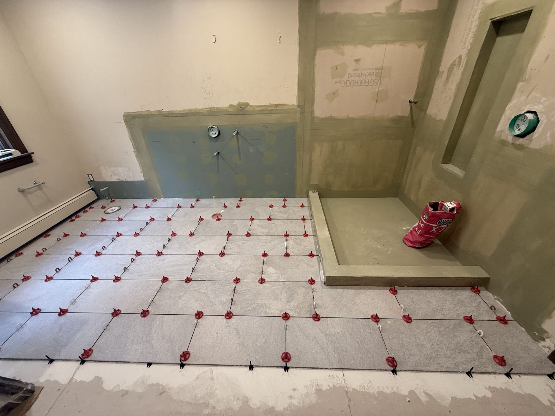 Bathroom in renovation with tiled floor, leveling system in place. Shower stall with a shoe. Walls unpainted.