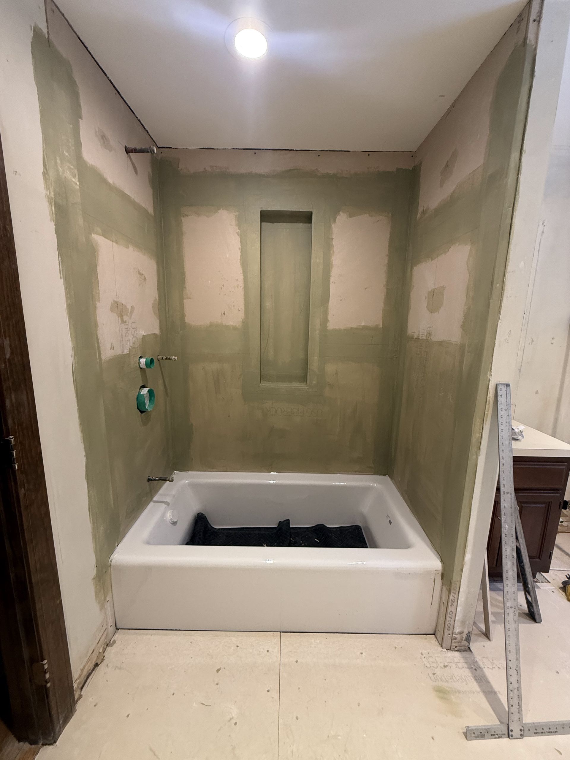 Bathroom remodel: white bathtub, green walls, recessed shelf, unfinished construction.