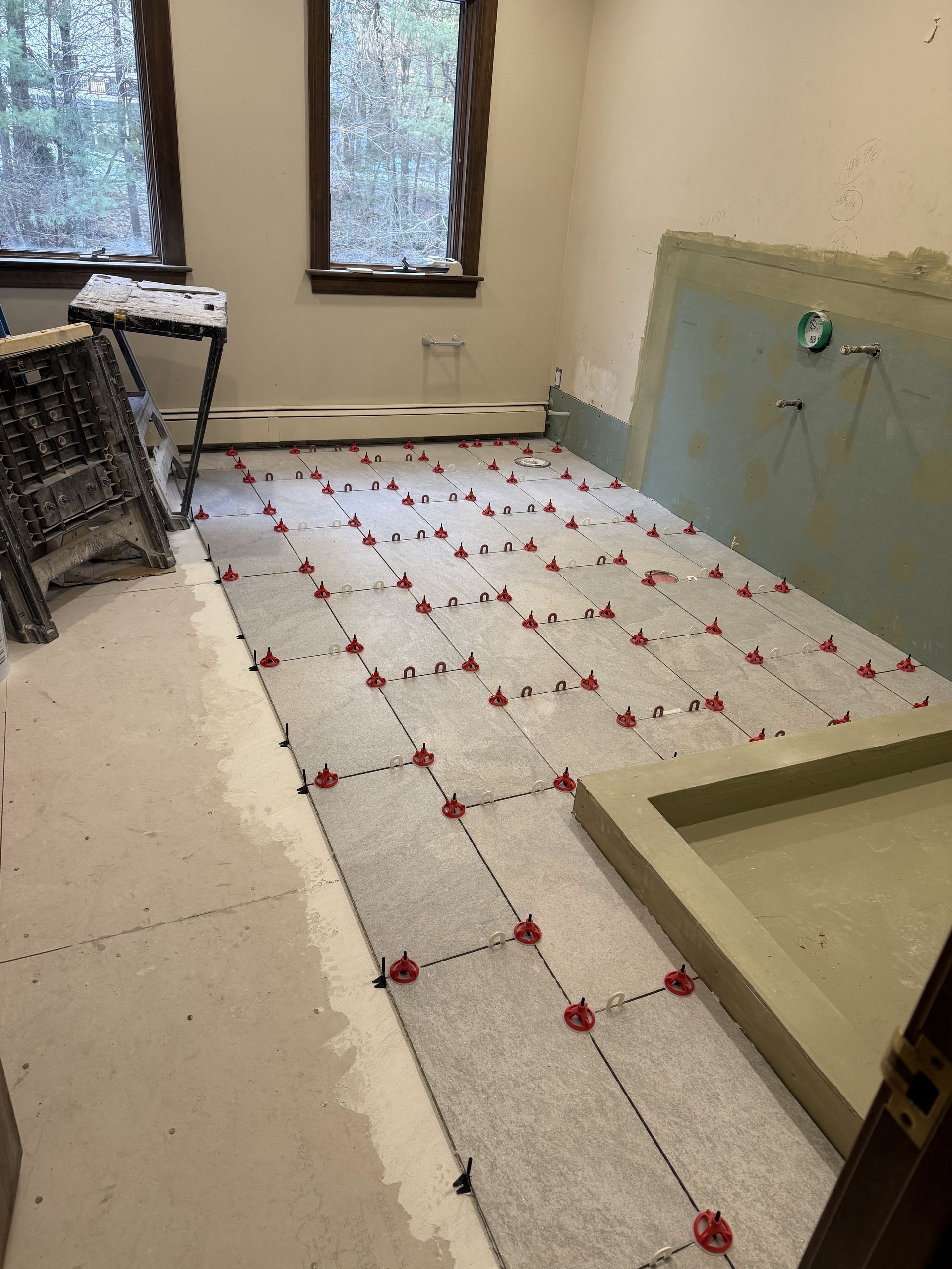 Bathroom floor under construction with gray tiles, spacers, and a built-in shower base.