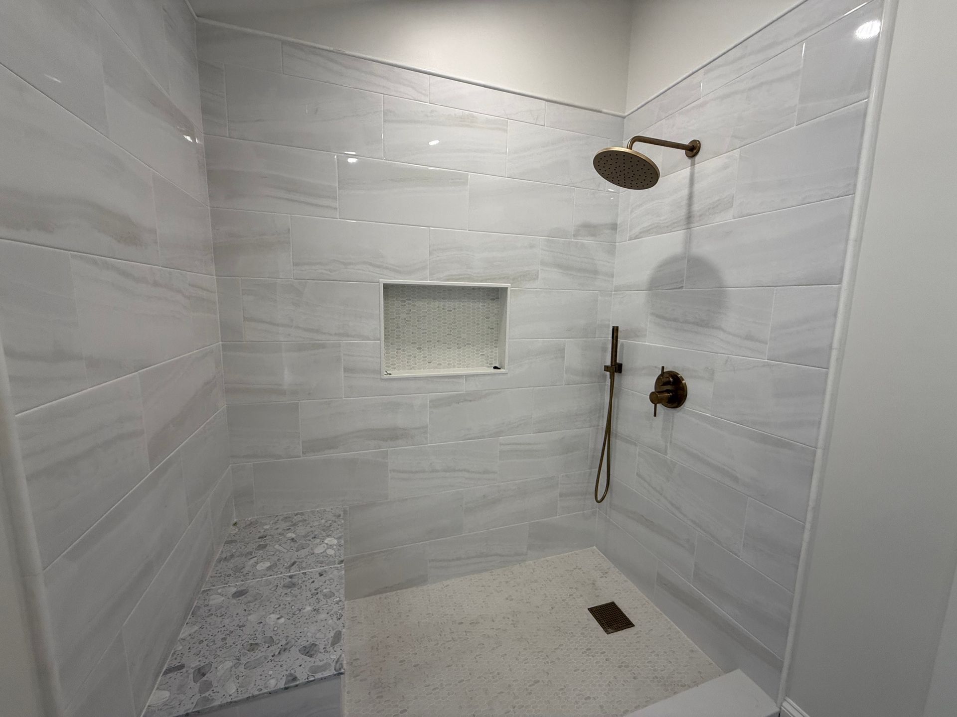 Tiled shower stall with bronze fixtures, a built-in bench, and a recessed shelf.