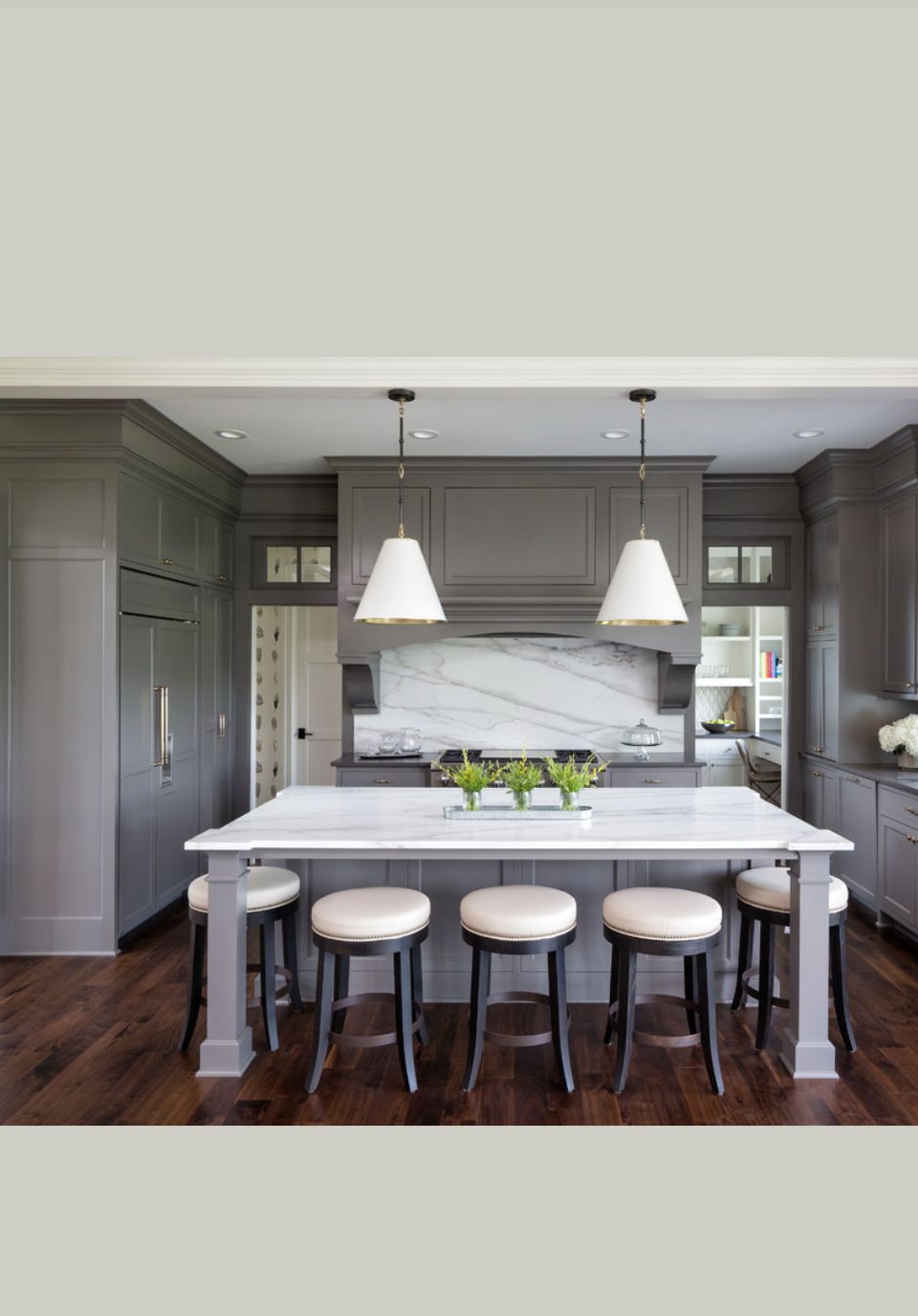 Gray kitchen with white marble island, stools, pendant lights, and wooden floor.