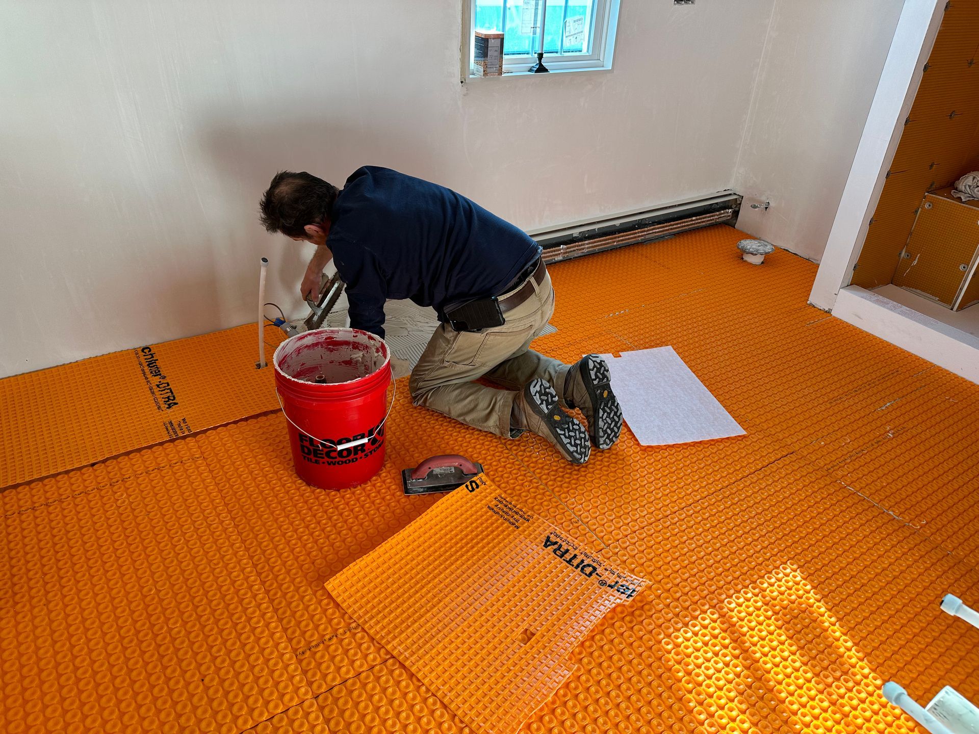 Man installing orange underfloor heating in a room; tools and materials are visible.