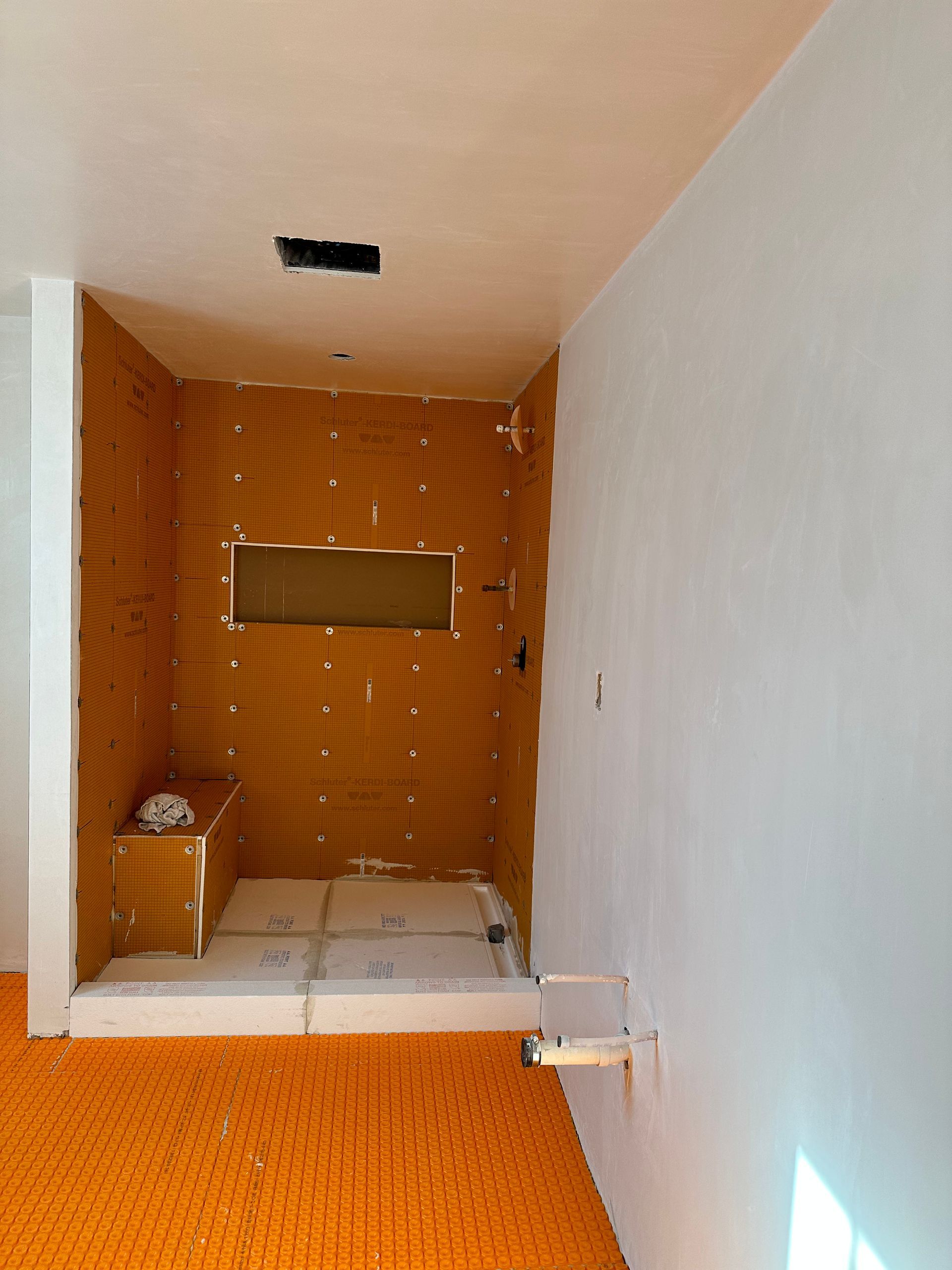 Bathroom under construction; orange tiled shower walls, white walls, and floor. Plumbing fixtures visible.