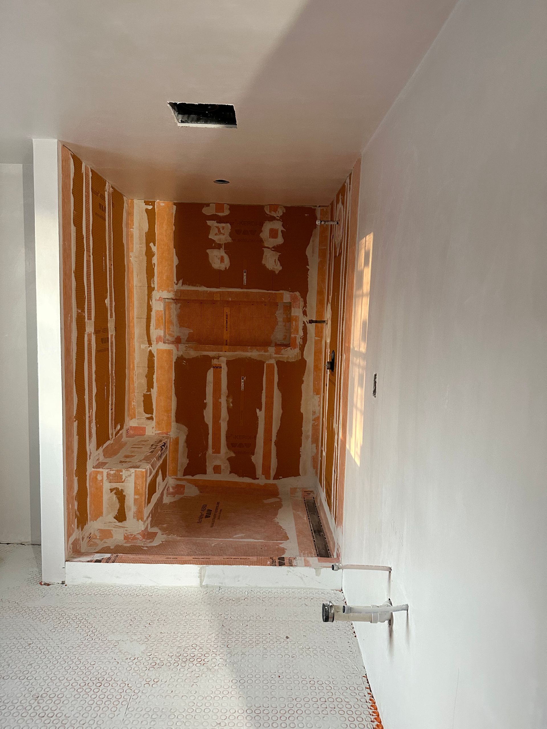 Bathroom construction: shower stall with exposed brick, white walls, and a plumbing fixture.