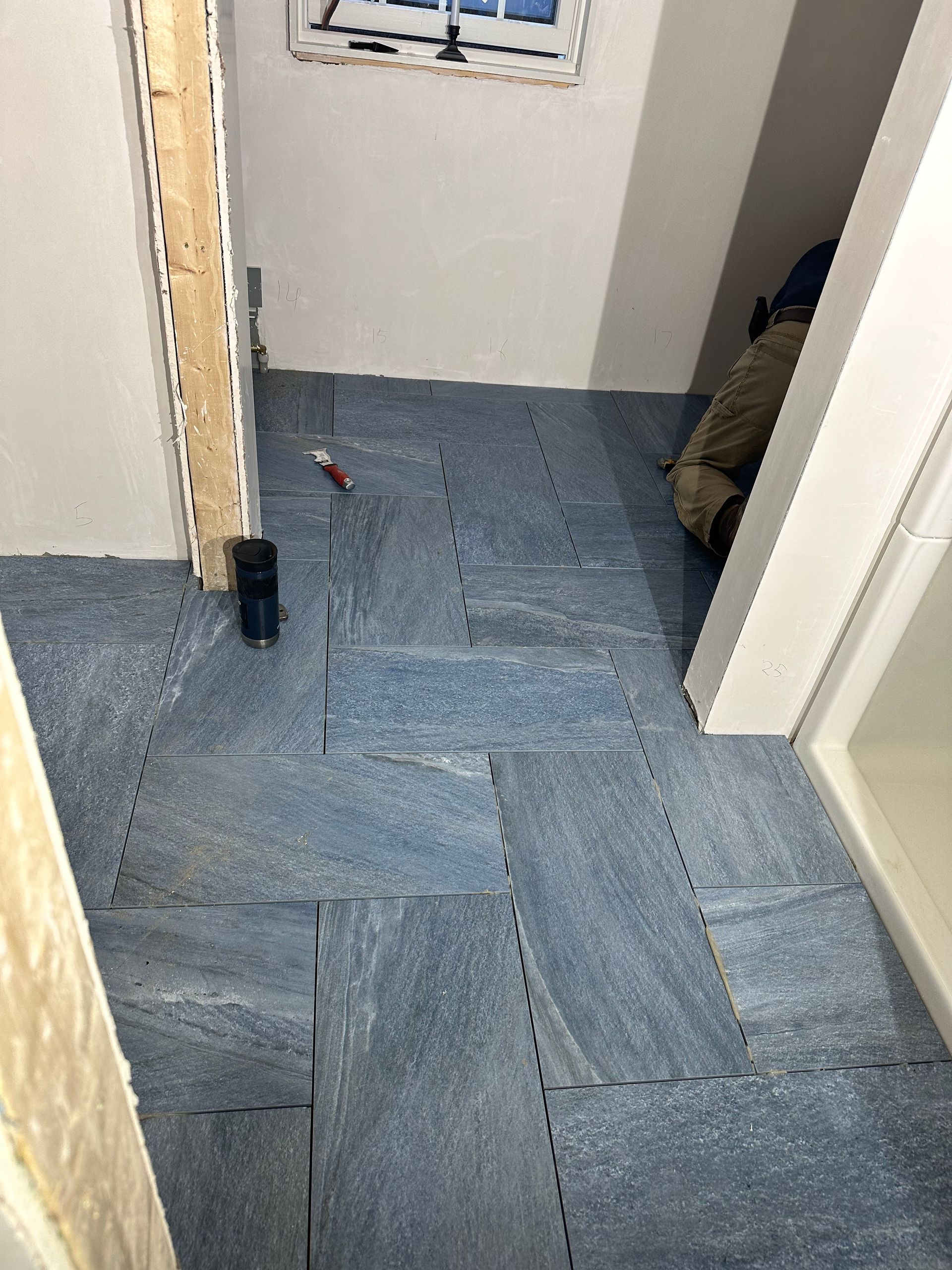 Bathroom floor with blue stone-like tiles, a worker, a window, and door frames visible.