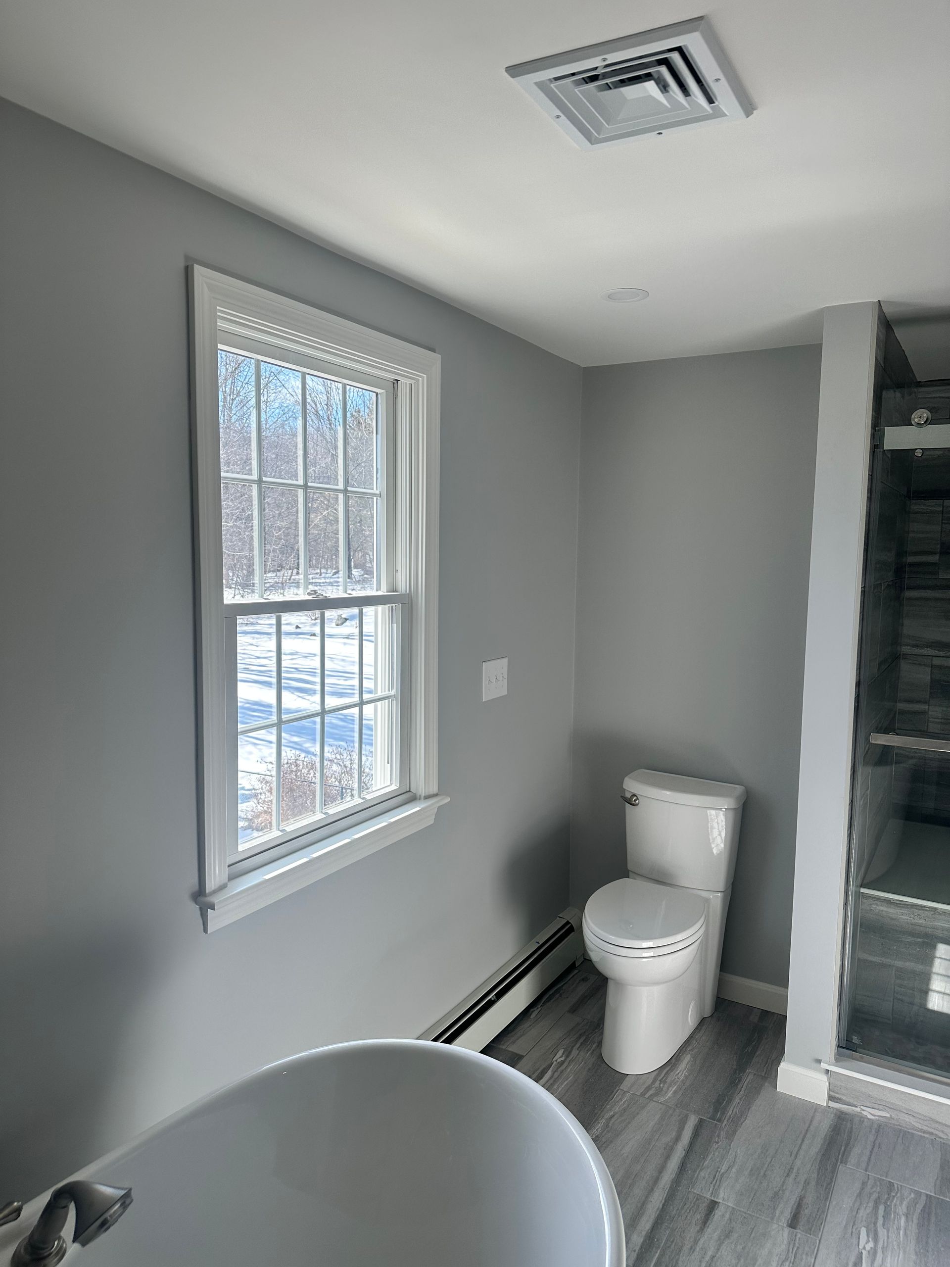 Bathroom with gray walls, white toilet, window, and a gray-plank floor.