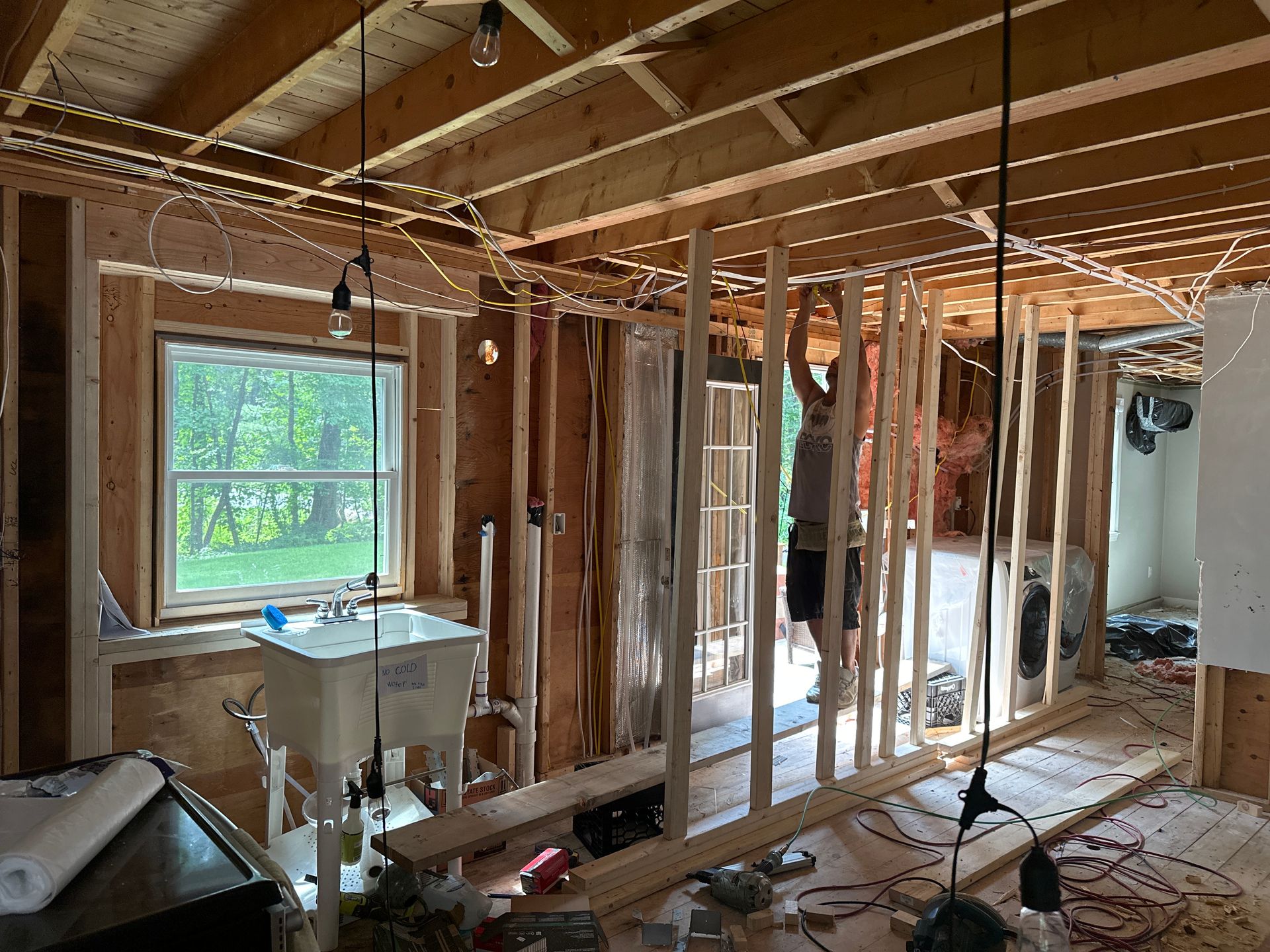Interior construction site with person framing a wall. Sink and window visible.