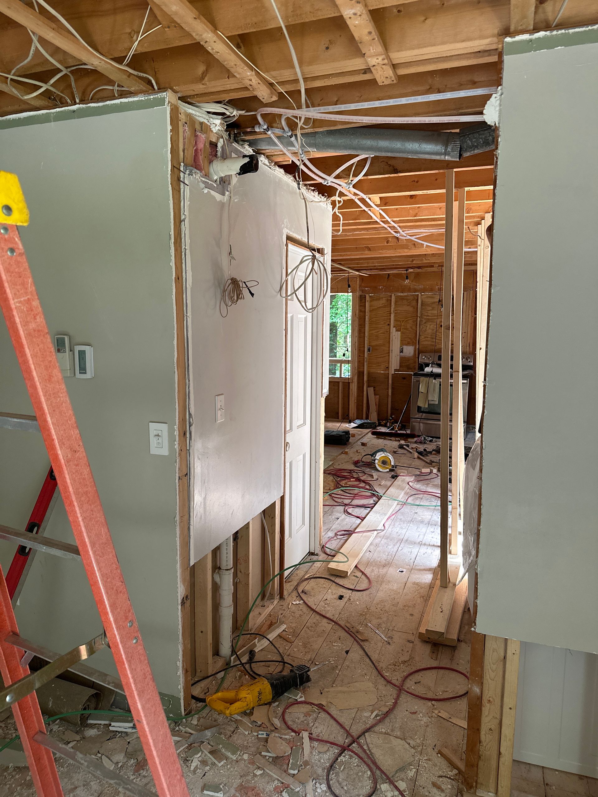 Interior construction site: walls with exposed studs, wiring, and ductwork. Orange ladder leans against a wall.