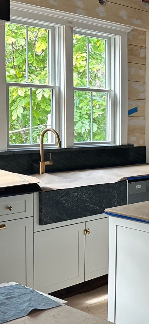 Kitchen with white cabinets, dark countertops, a window, and a gold faucet.