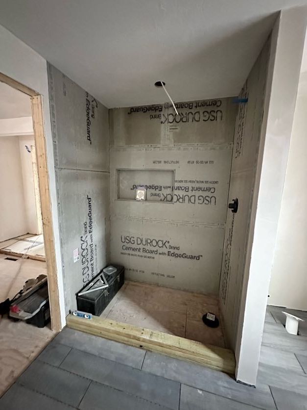 Shower stall under construction, gray cement board walls, wood base, niche, and drain.