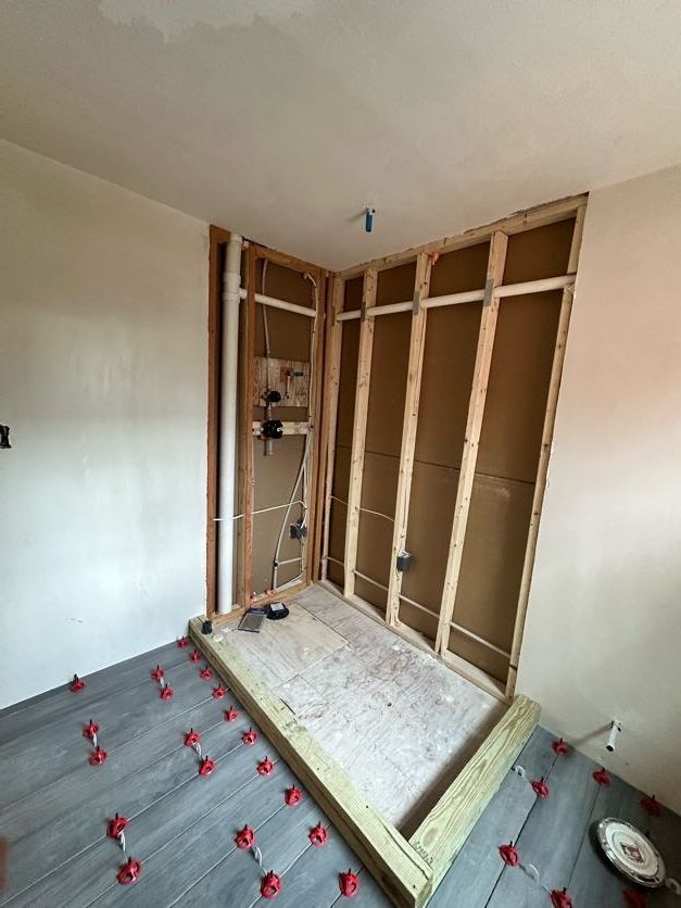 Bathroom renovation in progress: framed shower stall with plumbing and electrical, gray floor tiles, and unfinished walls.