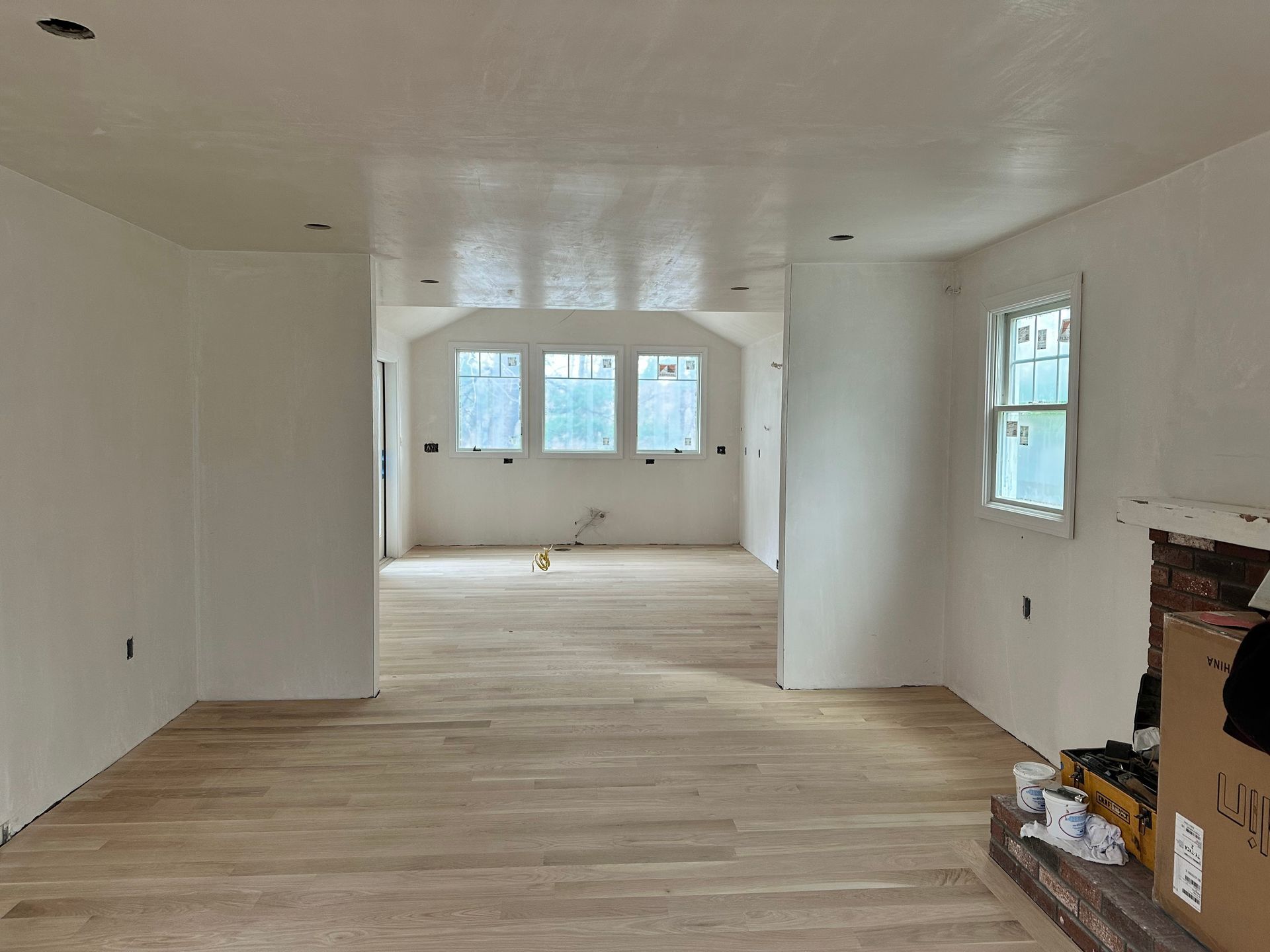Interior view of a room under construction with new light wood flooring, white walls and ceiling.