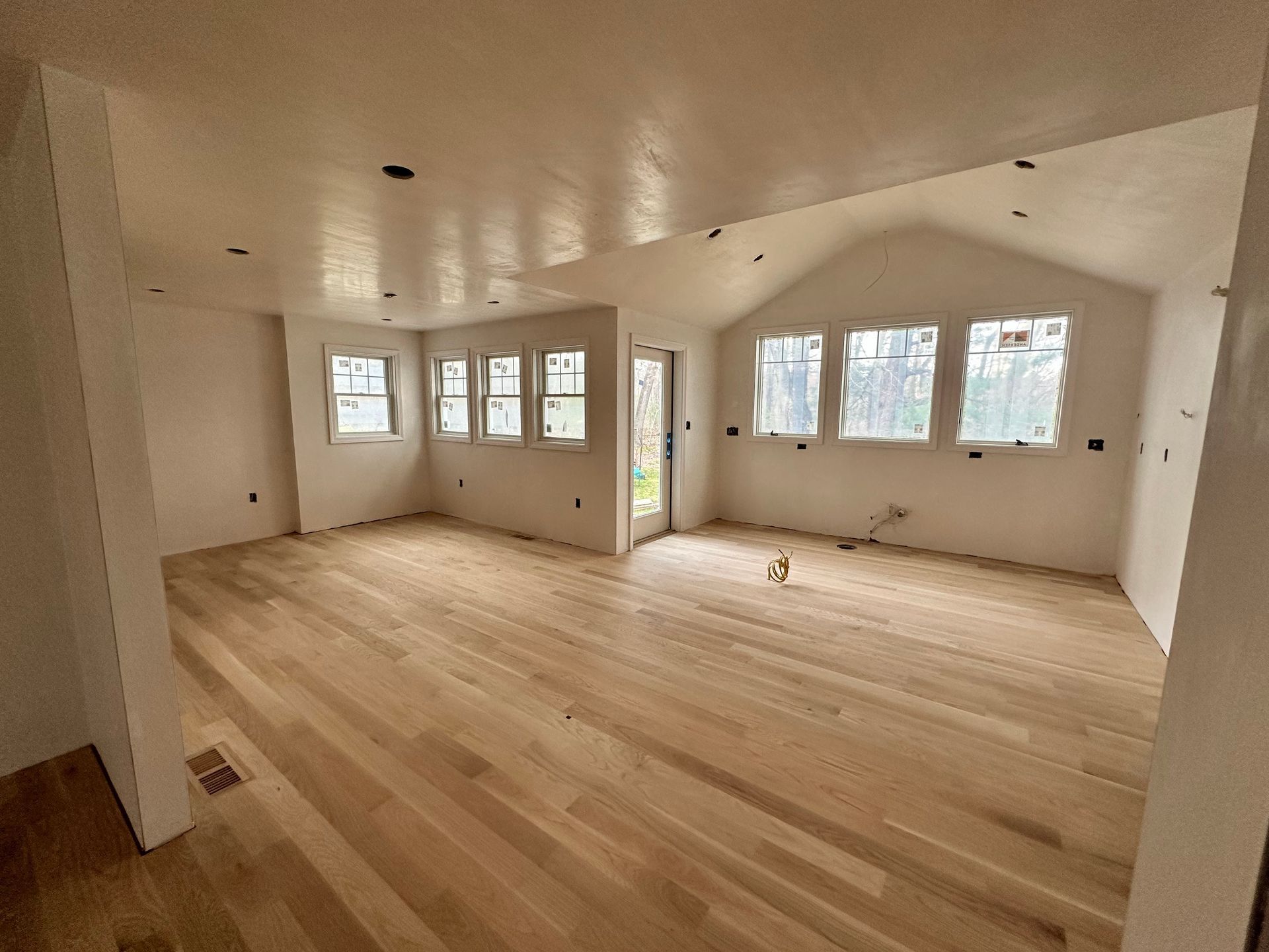 Empty room with light wood floors, white walls, and multiple windows.