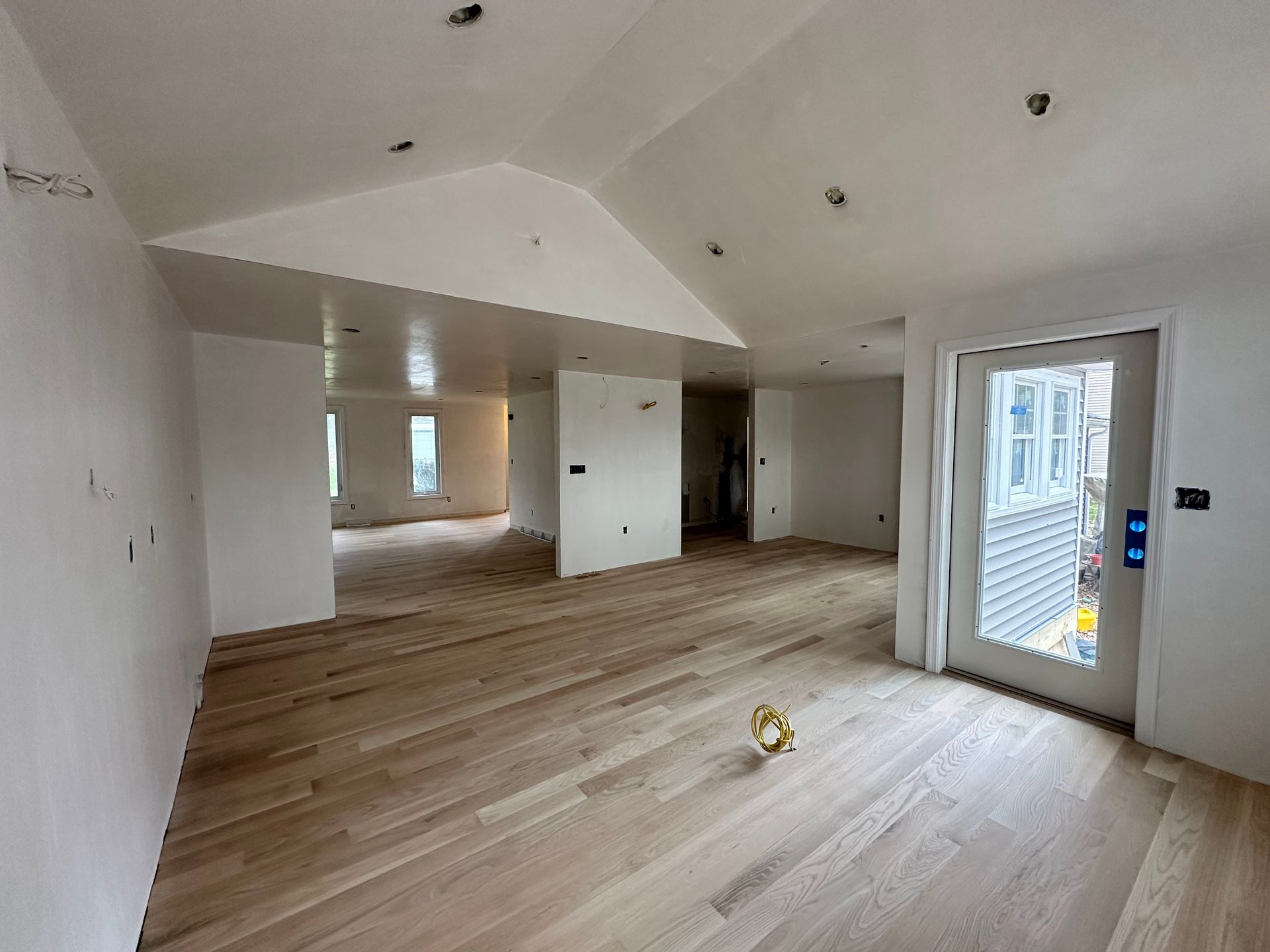 Interior of a room under construction with light wood flooring, white walls, and a glass door.