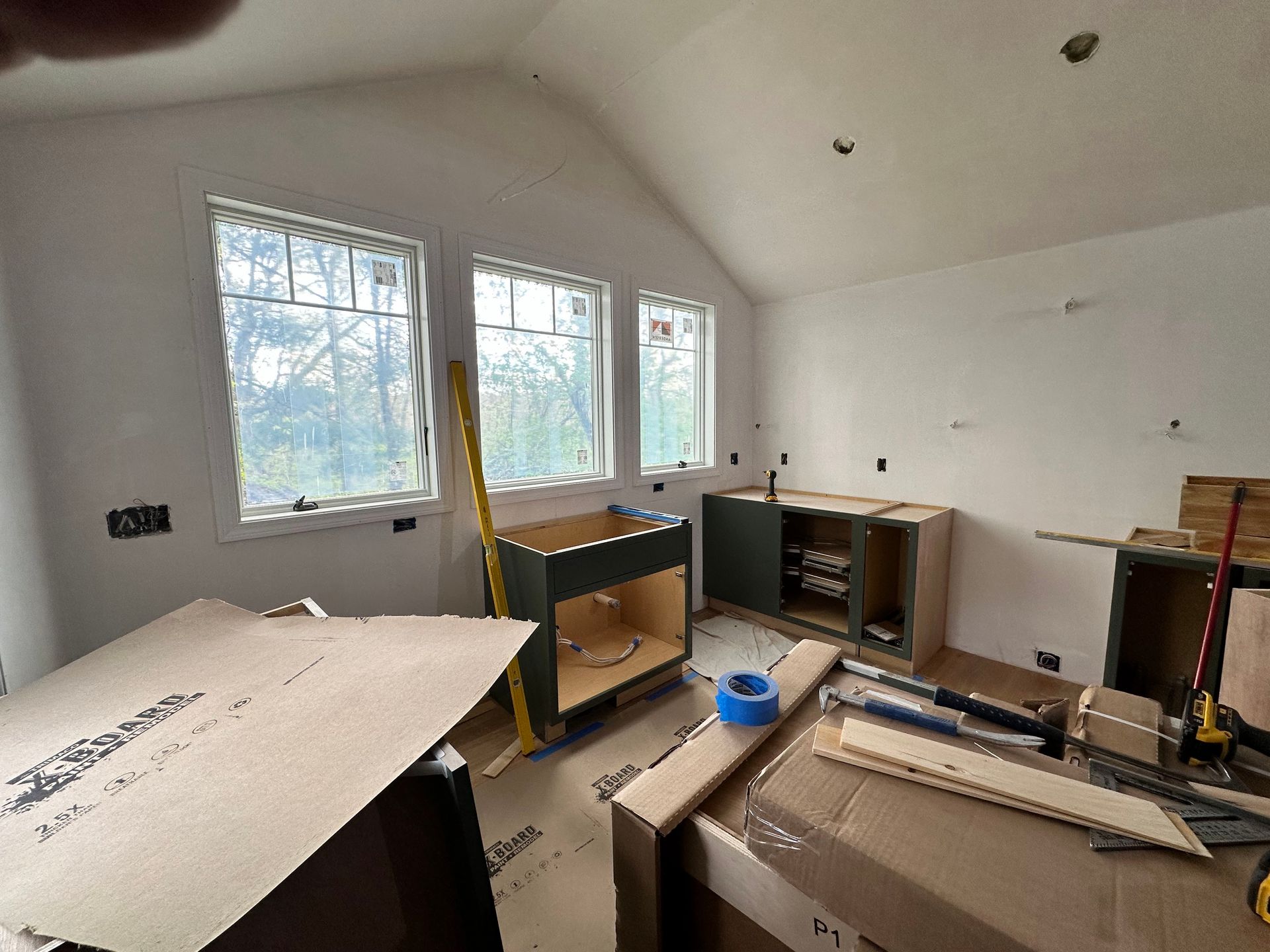 Kitchen under construction with unfinished cabinets and windows.