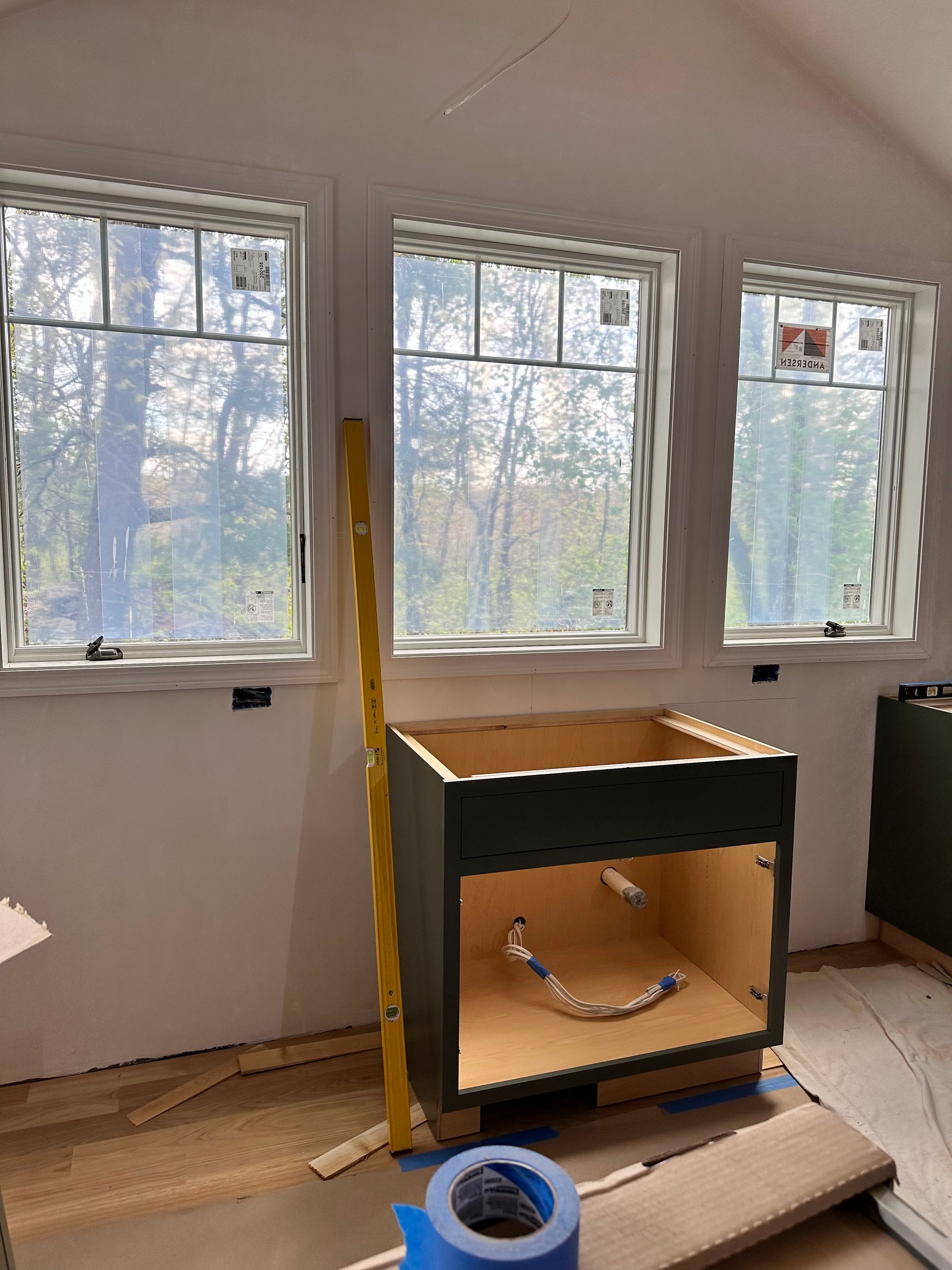 Interior kitchen construction: dark green cabinet under three windows; level propped against it.