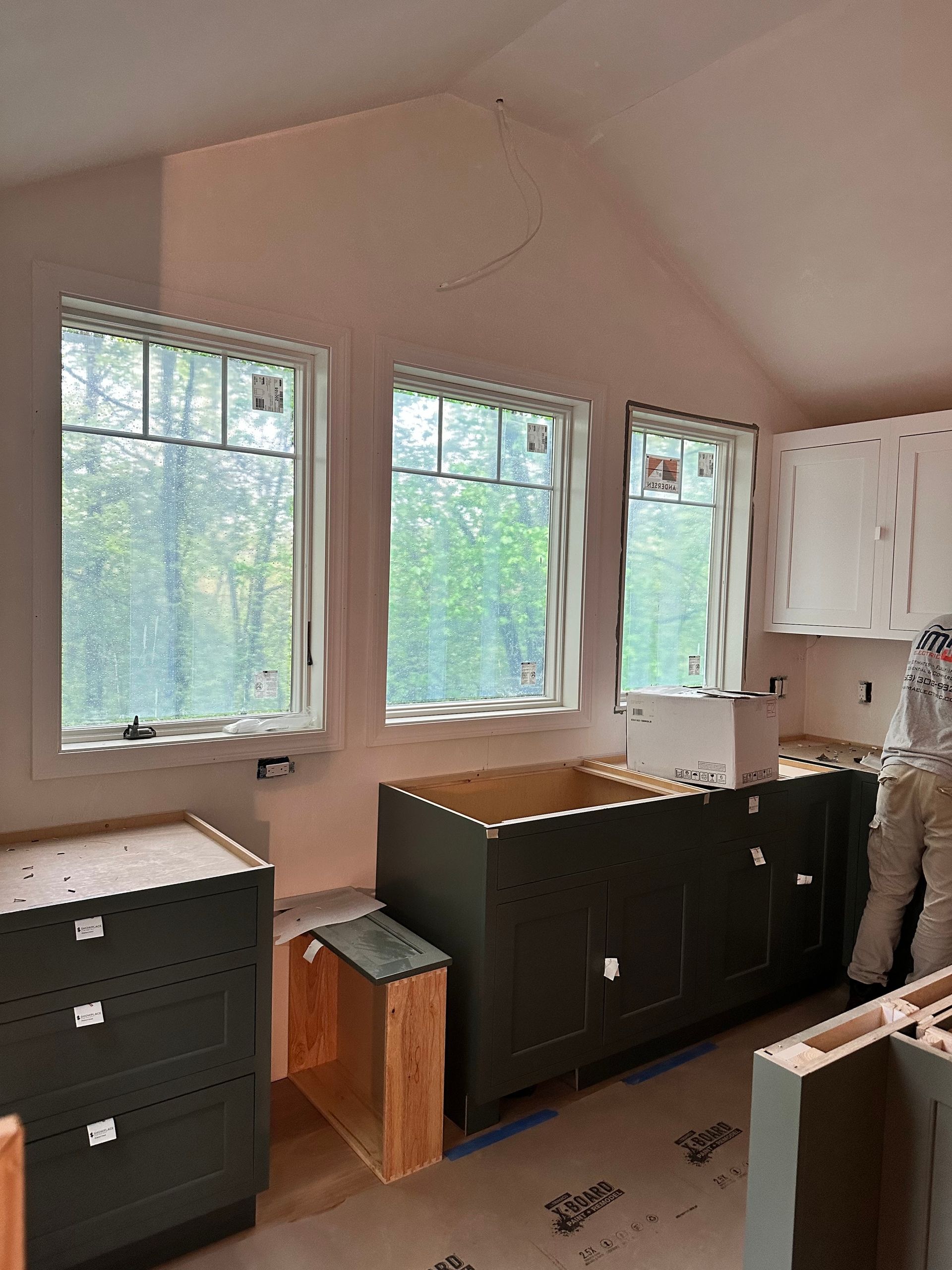 Kitchen under construction with cabinets and windows. Green cabinets, white upper cabinets, light pink walls, and three windows.