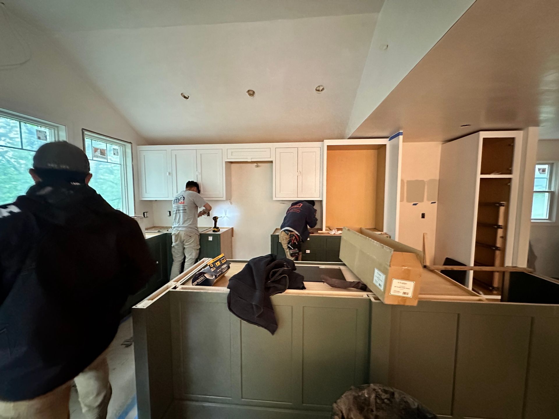 Men installing kitchen cabinets in a room with green island and white walls.
