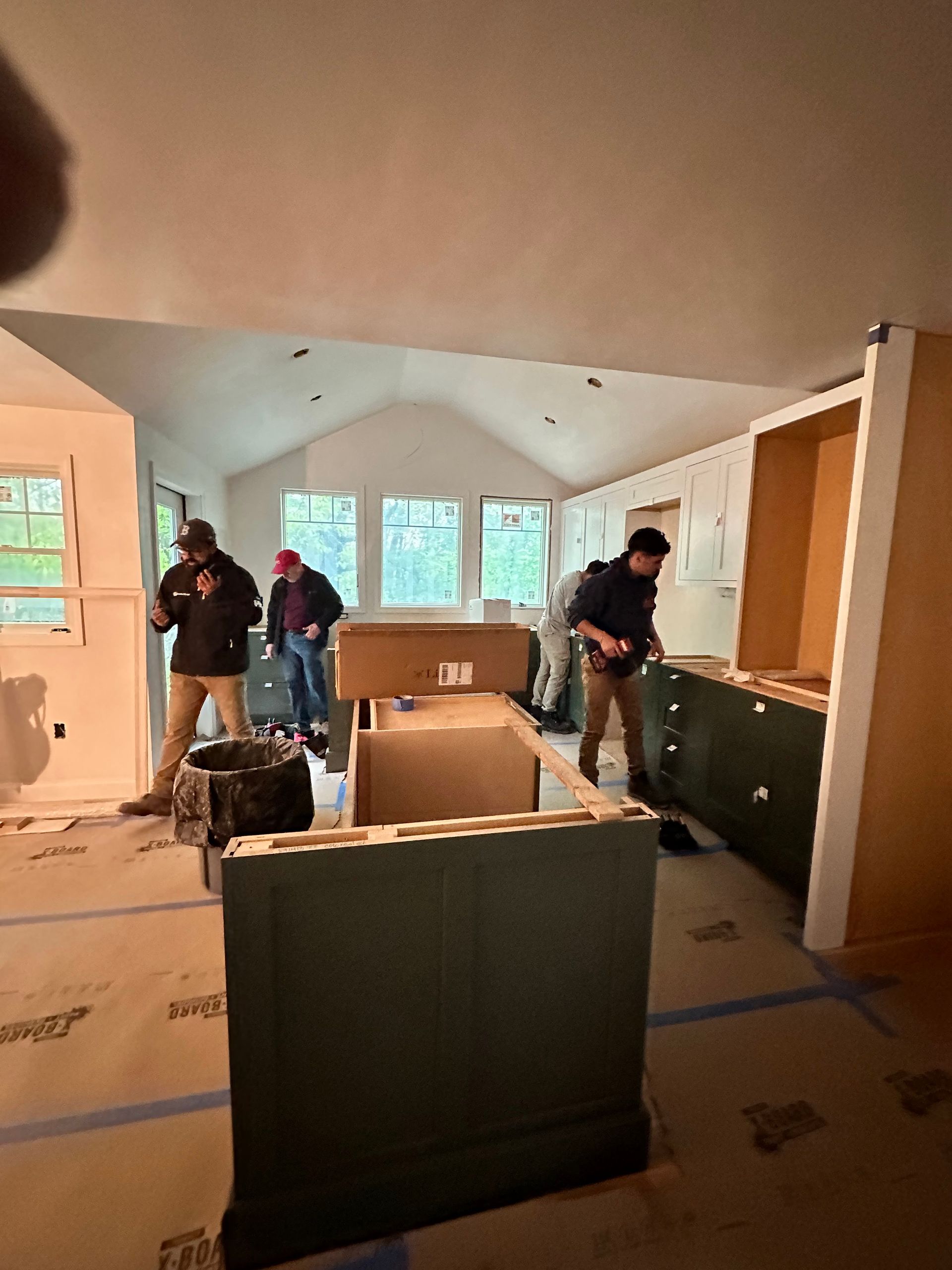 People installing cabinets in a kitchen with a vaulted ceiling. The cabinets are green.