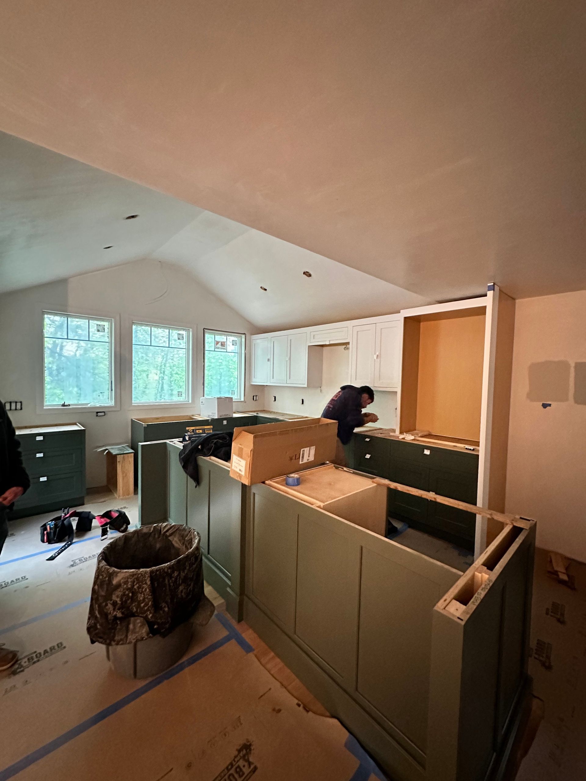 Kitchen under construction with green cabinets, a person working, and natural light.