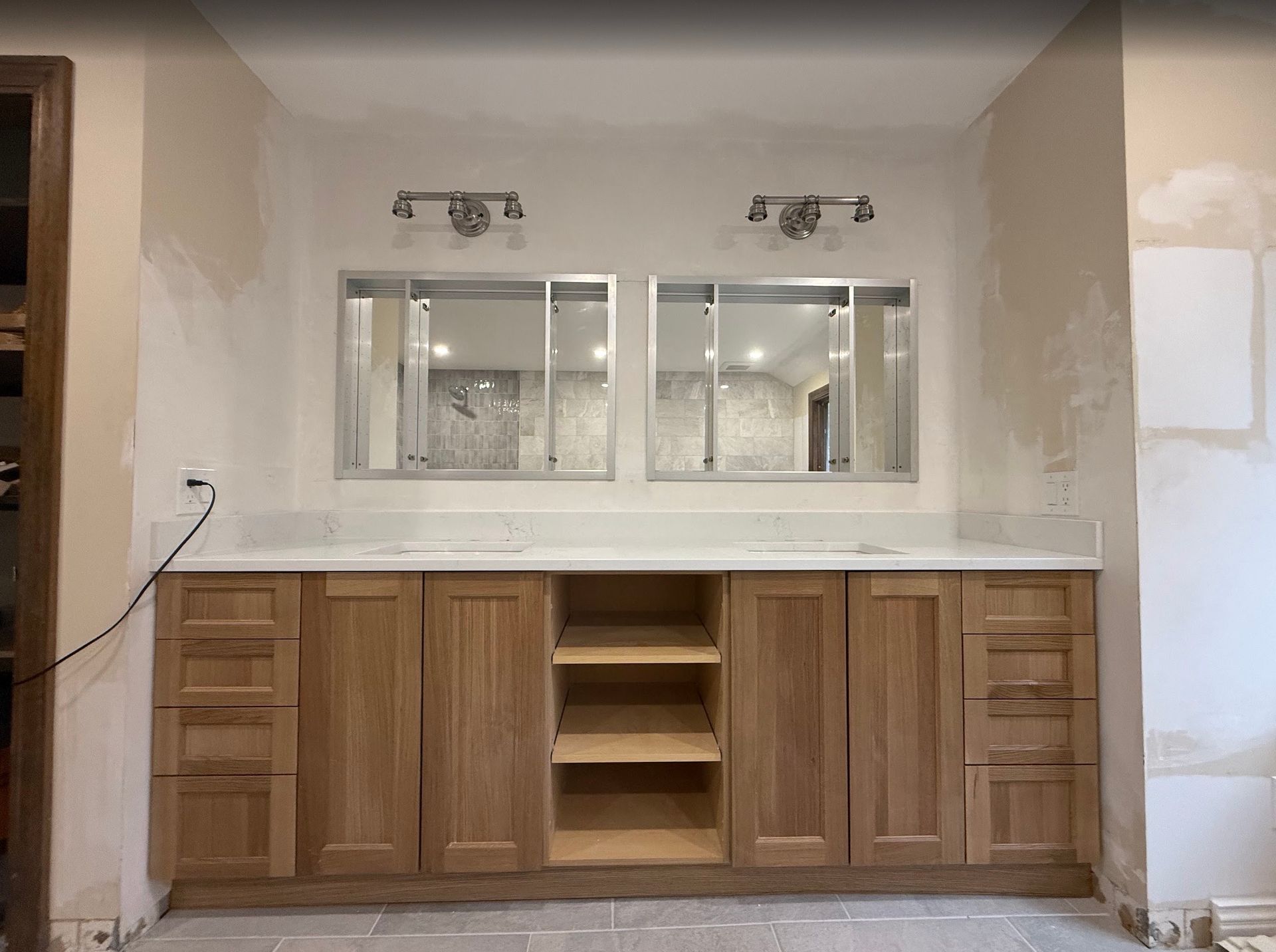 Bathroom vanity with two mirrors, light fixtures, and a marble countertop. Oak cabinets are installed.