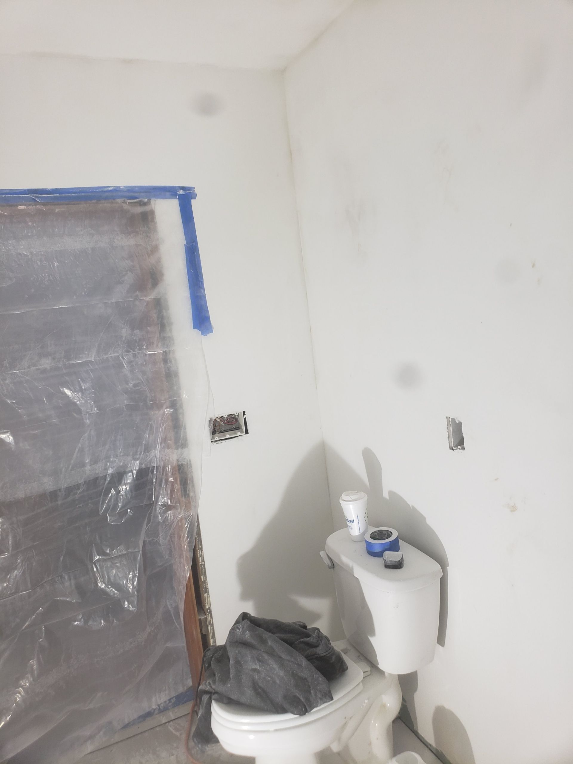Bathroom under renovation with white walls, a toilet, and plastic sheeting over a door.