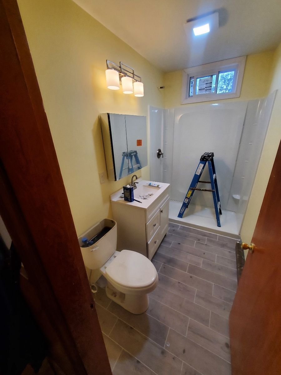 Bathroom remodel with new vanity, shower, and toilet. Ladder is in the shower. Yellow walls and gray tiled floor.