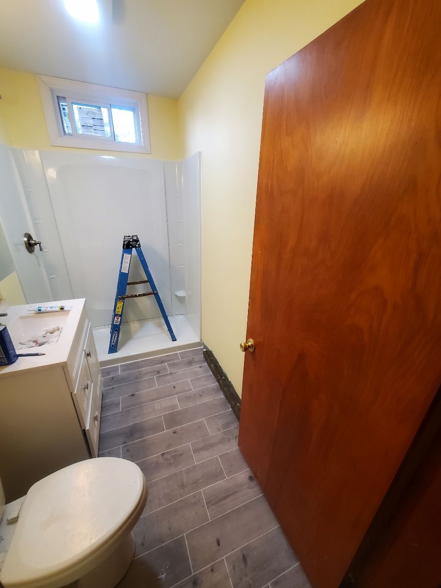 Bathroom with toilet, vanity, shower, and a ladder inside. Gray flooring and yellow walls.
