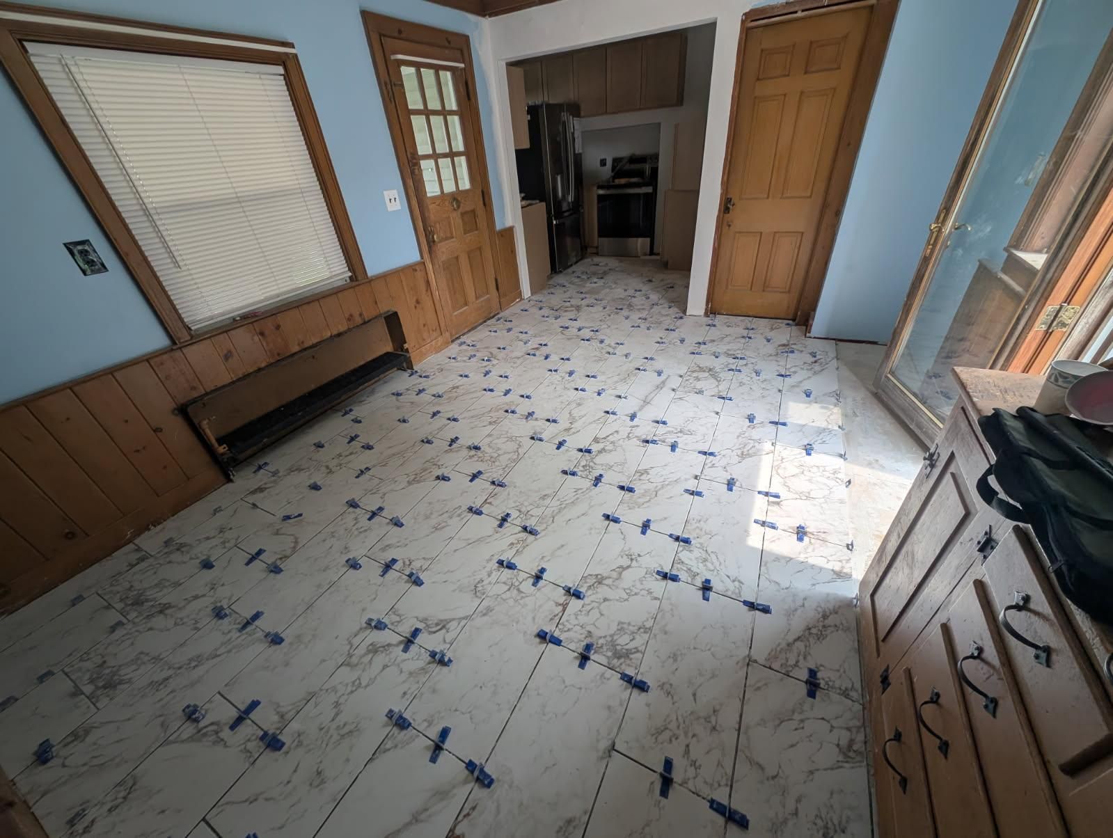 Interior room with new white and gray patterned flooring, wooden doors, and blue walls.