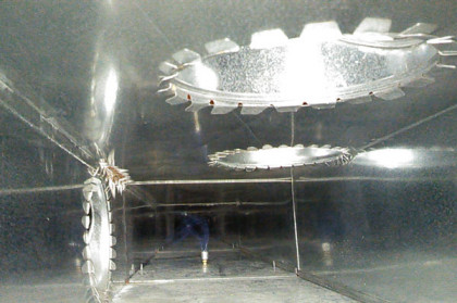 Industrial interior with reflective metal walls and a large round overhead light fixture.