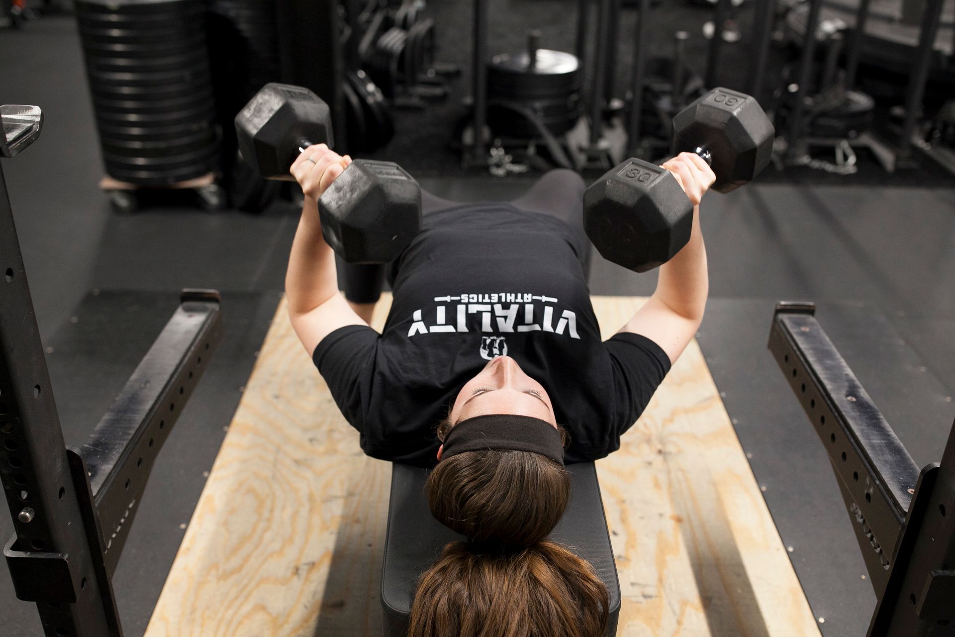 Person doing dumbbell chest press on a weight bench in a gym.