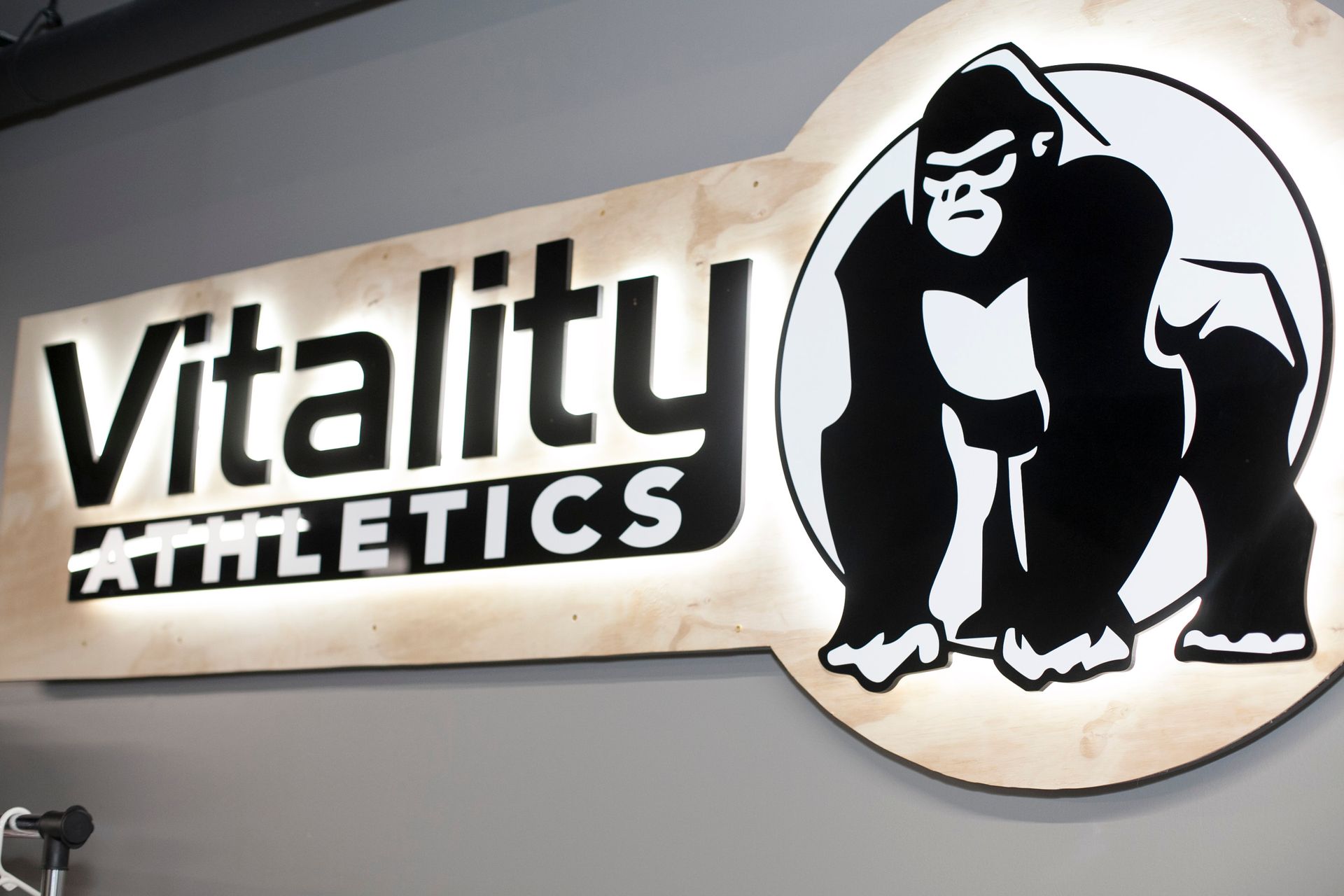 Sign for Vitality Athletics: Illuminated text and gorilla logo on a light-colored background.