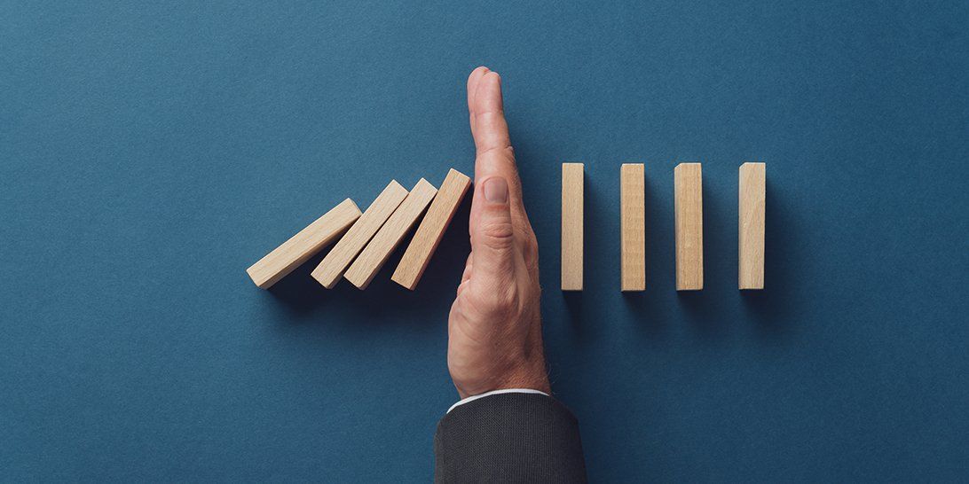 A hand is stopping a row of wooden dominoes from falling.