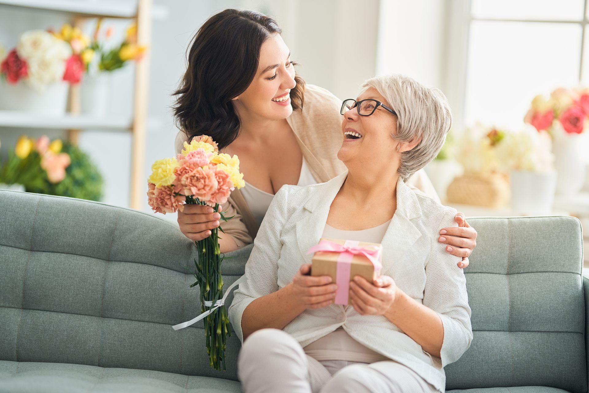 A woman is giving a gift to an older woman who is  sitting on a sofa.