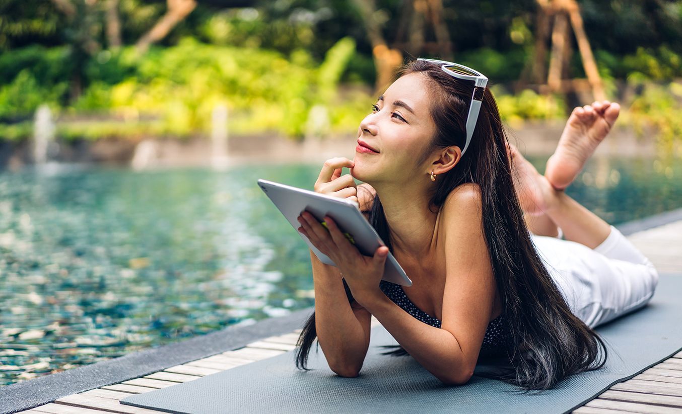 A girl have a tablet laying near swimming pool