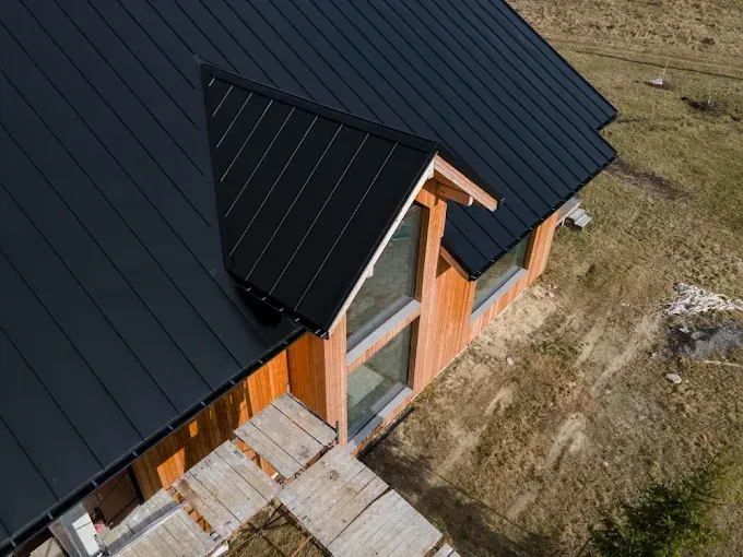 Black metal roof on a wood-sided building with large windows, set on a grassy plot.