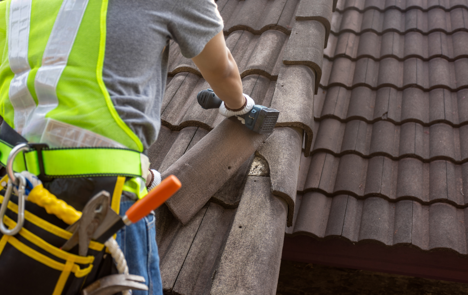 Roofer, wearing safety gear, replacing a tile on a brown tiled roof.